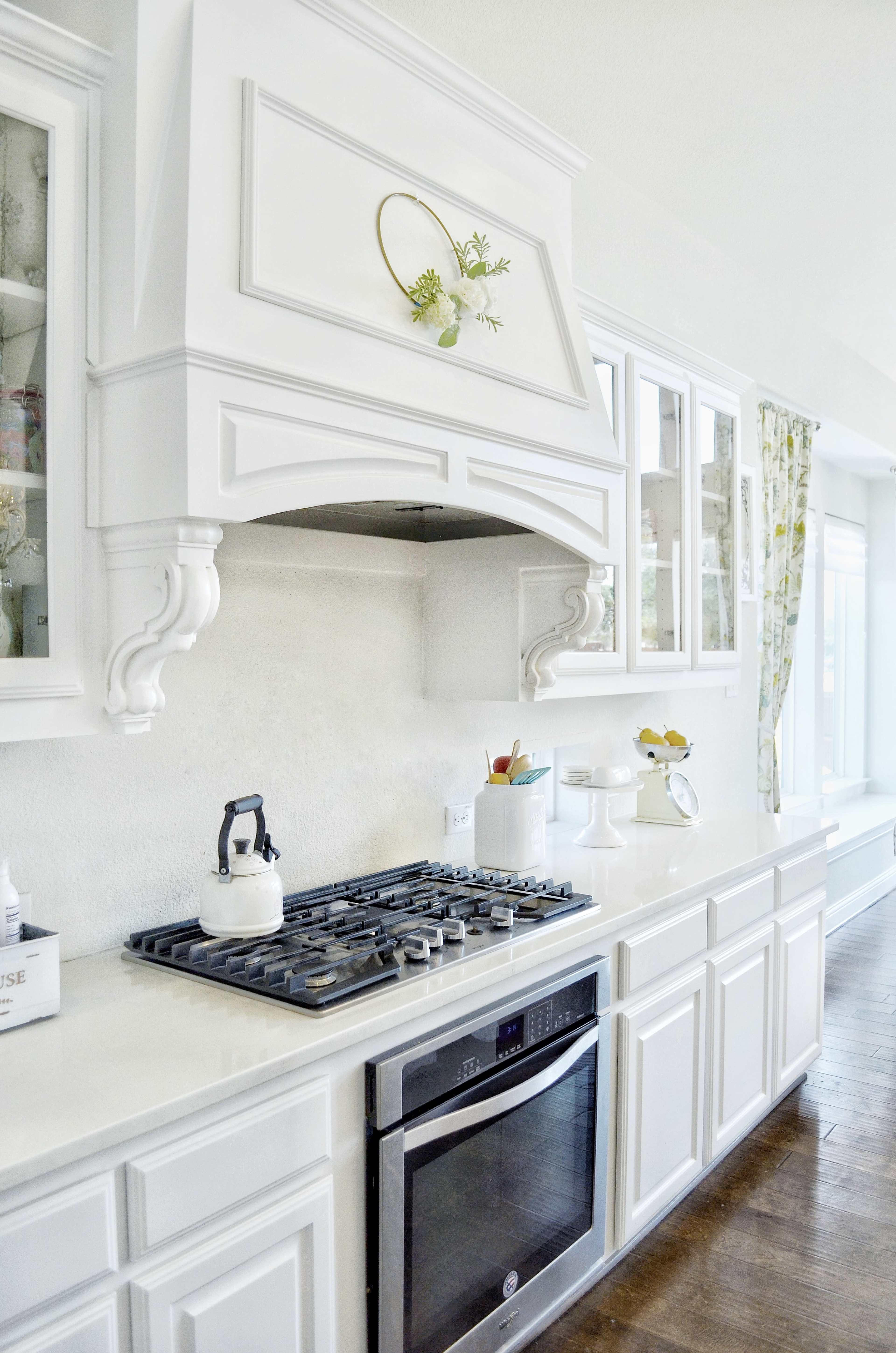 A modern kitchen with white cabinetry, a gas stove, and a decorative hood embellished with greenery.