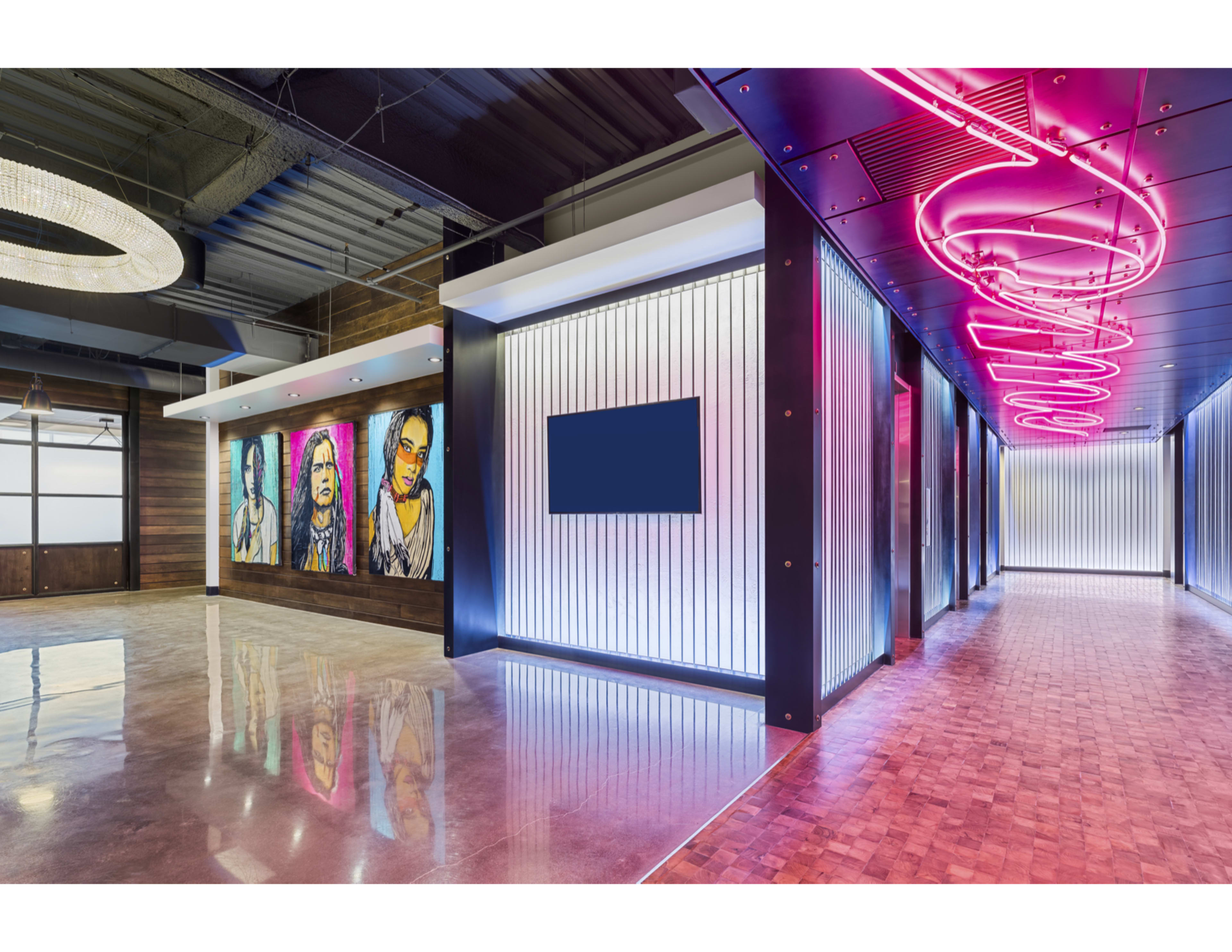 A modern hallway with metallic walls, colorful artwork depicting faces, and neon signage illuminating the space.