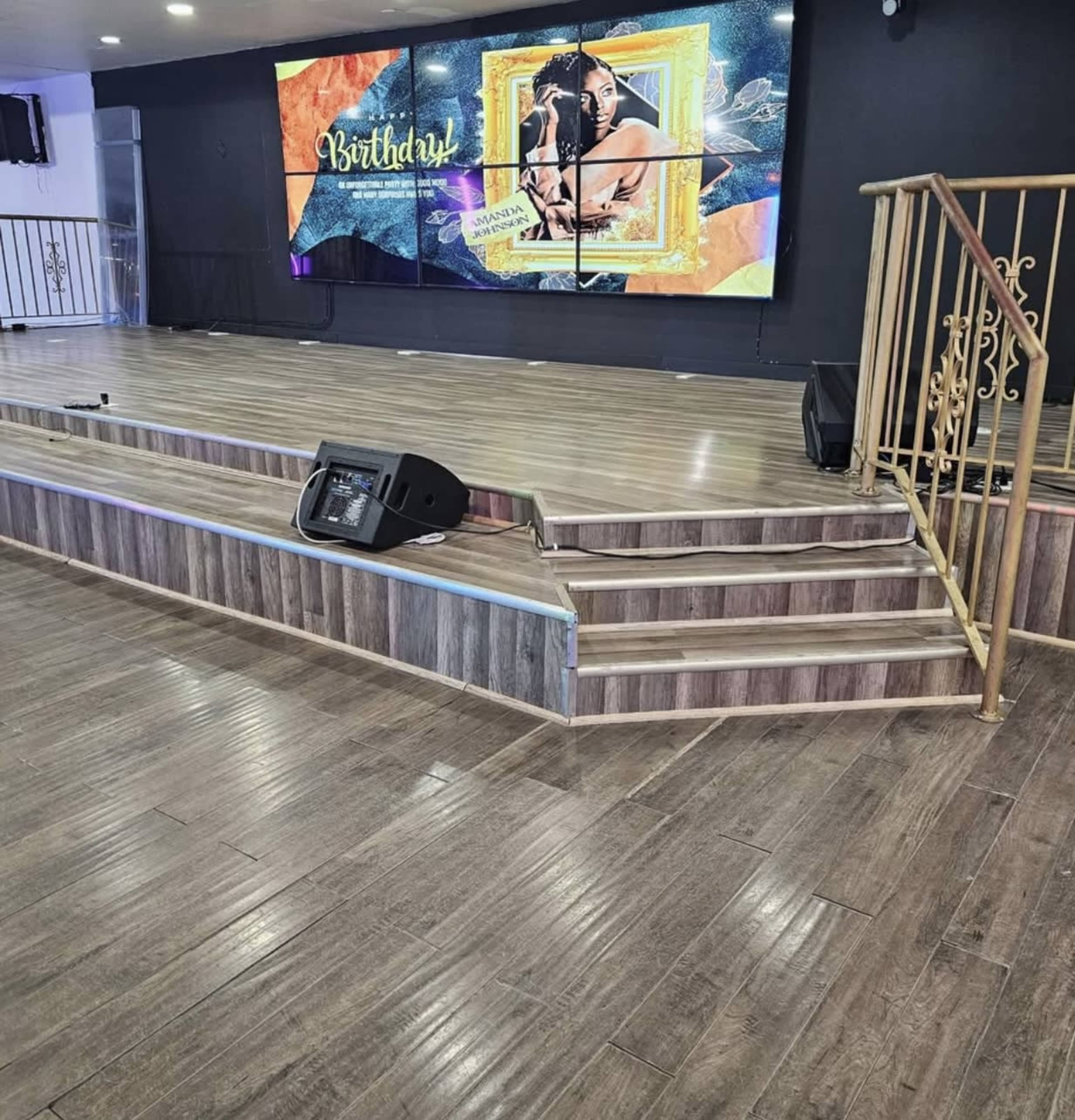 The image shows a stage area with wooden flooring, a staircase leading up, and a large digital display featuring a birthday celebration theme.