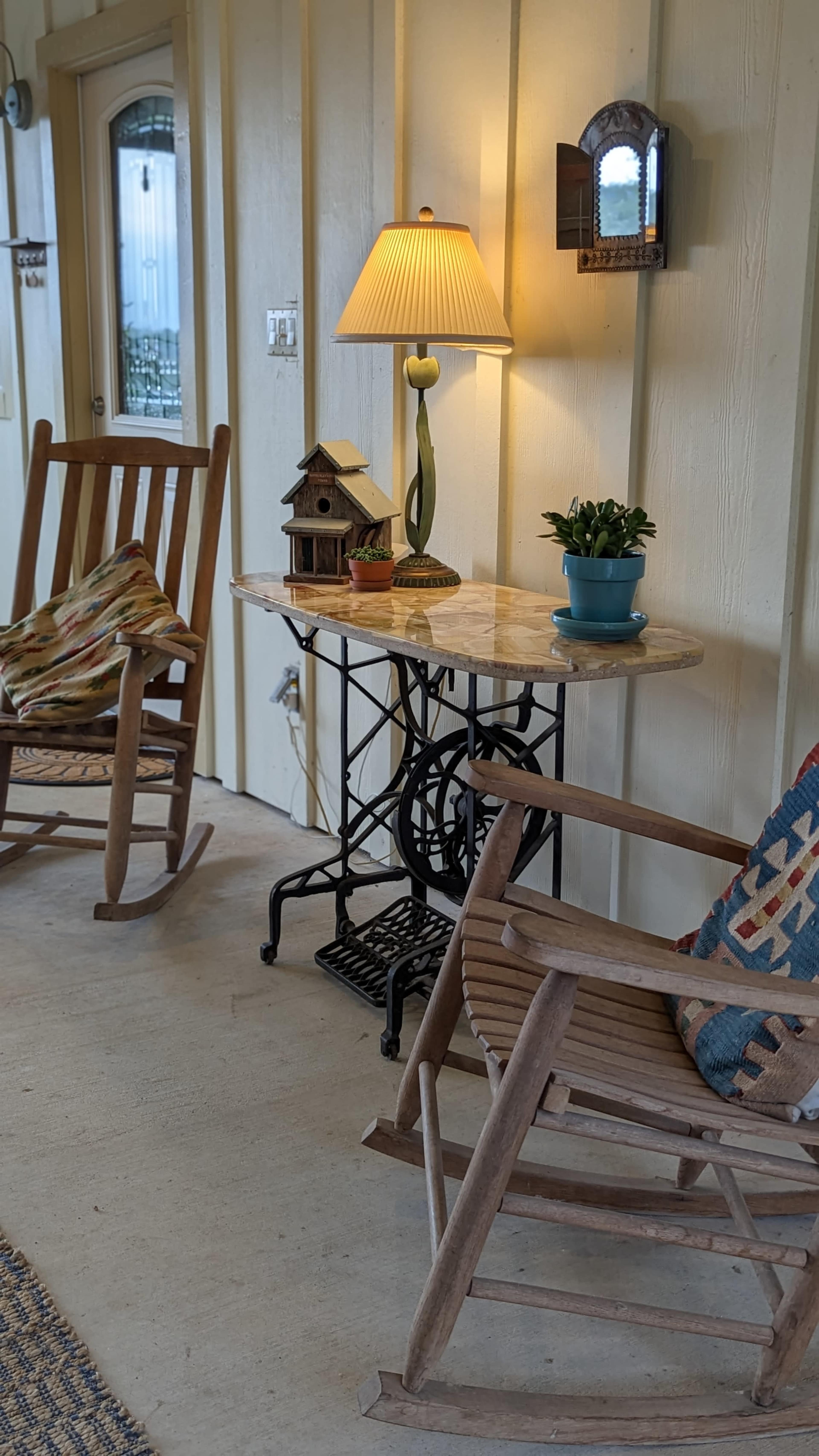 A porch area with two rocking chairs, a small table with a lamp and a potted plant, and a decorative birdhouse.