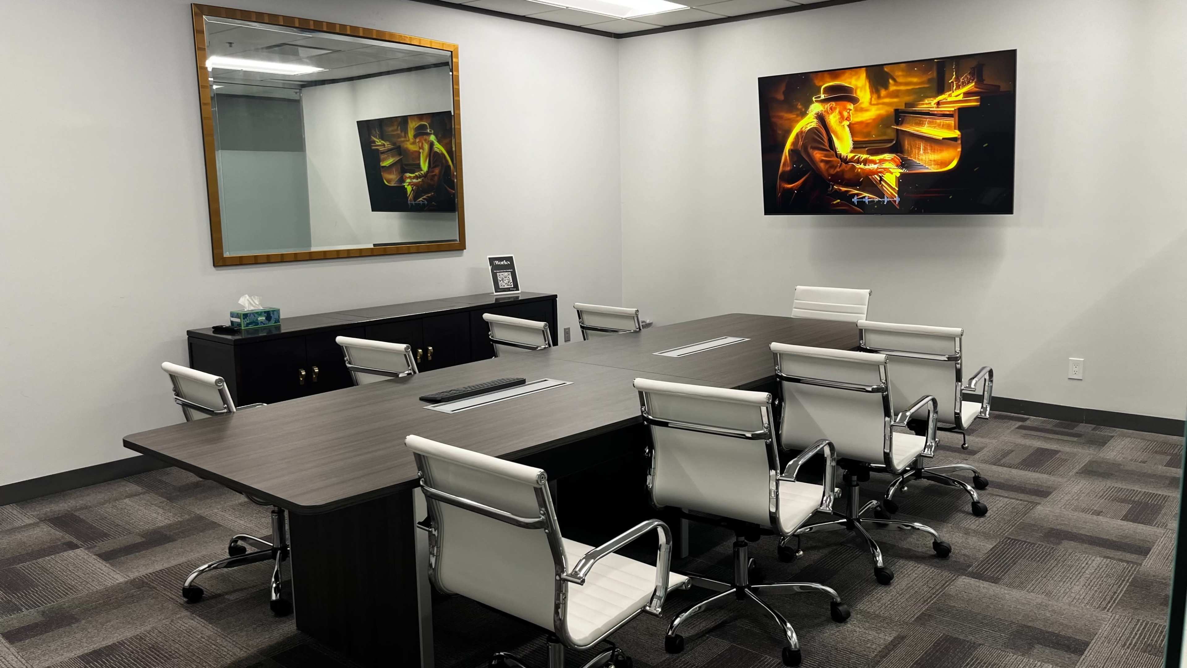 A modern conference room features a large table surrounded by white chairs, a wall-mounted painting of a pianist, and a mirror.