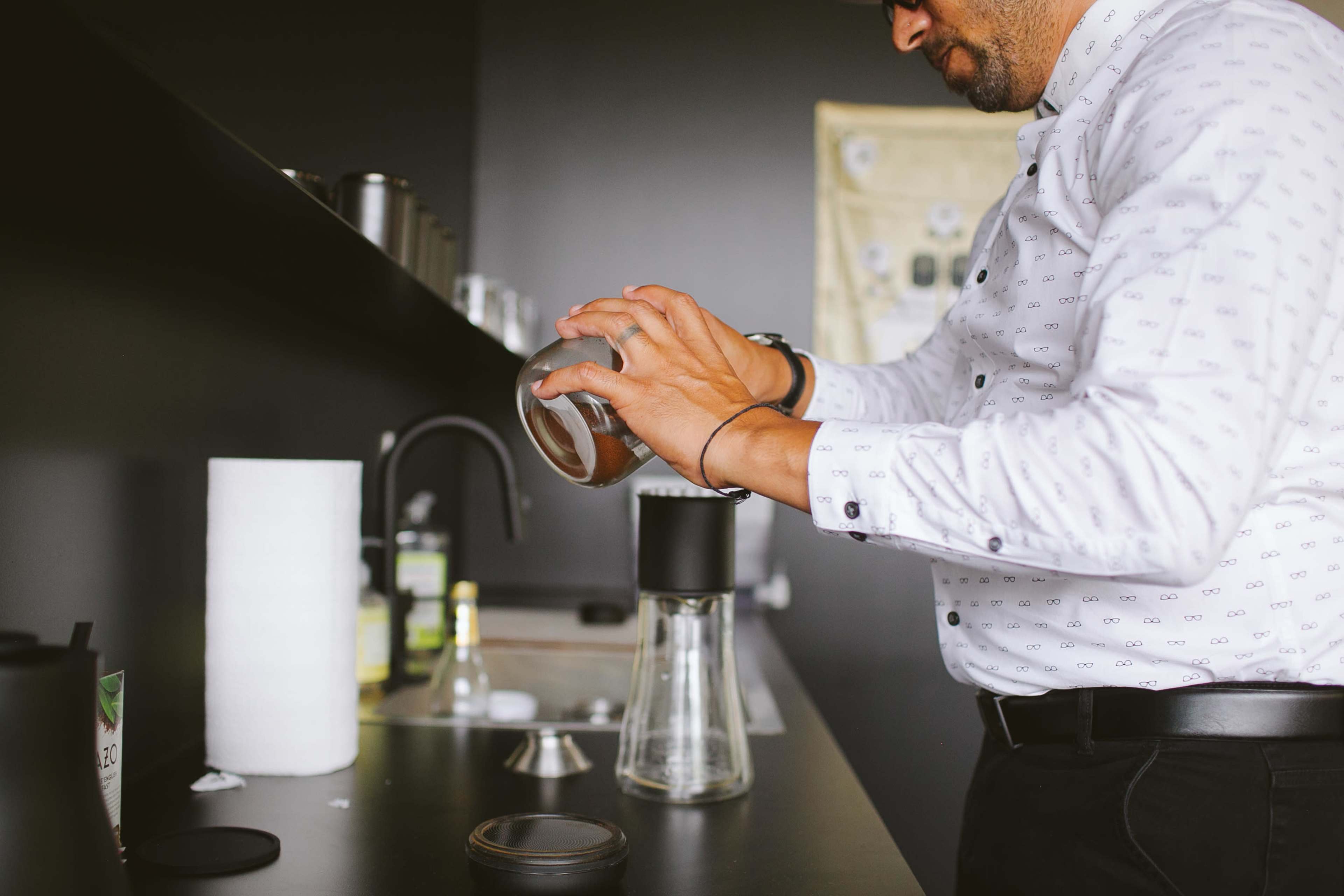 A man is pouring coffee grounds into a coffee maker on a black countertop.