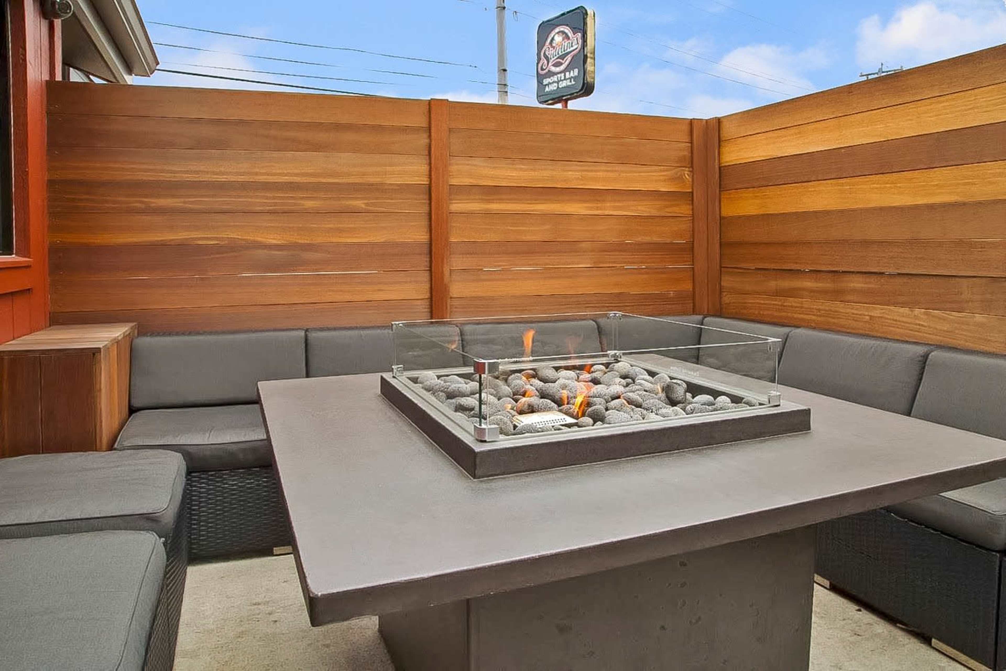 A patio setup featuring a modern fire pit surrounded by gray seating and wooden privacy panels.