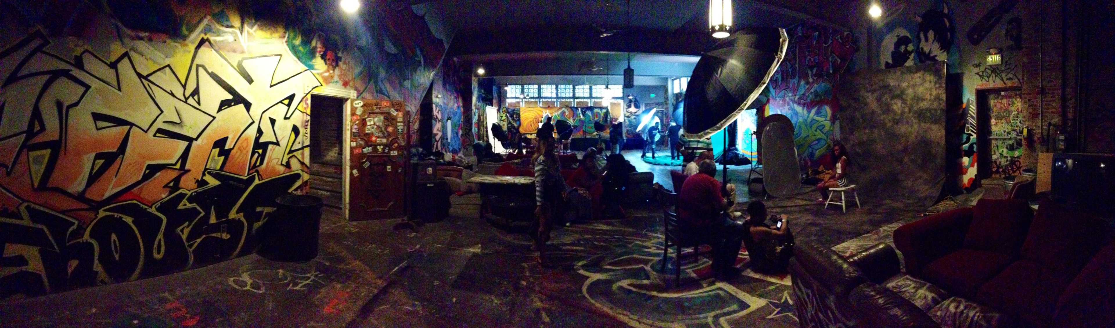 A vibrant indoor space filled with graffiti art, featuring a group of people engaging in activities around a central area illuminated by colorful lights.