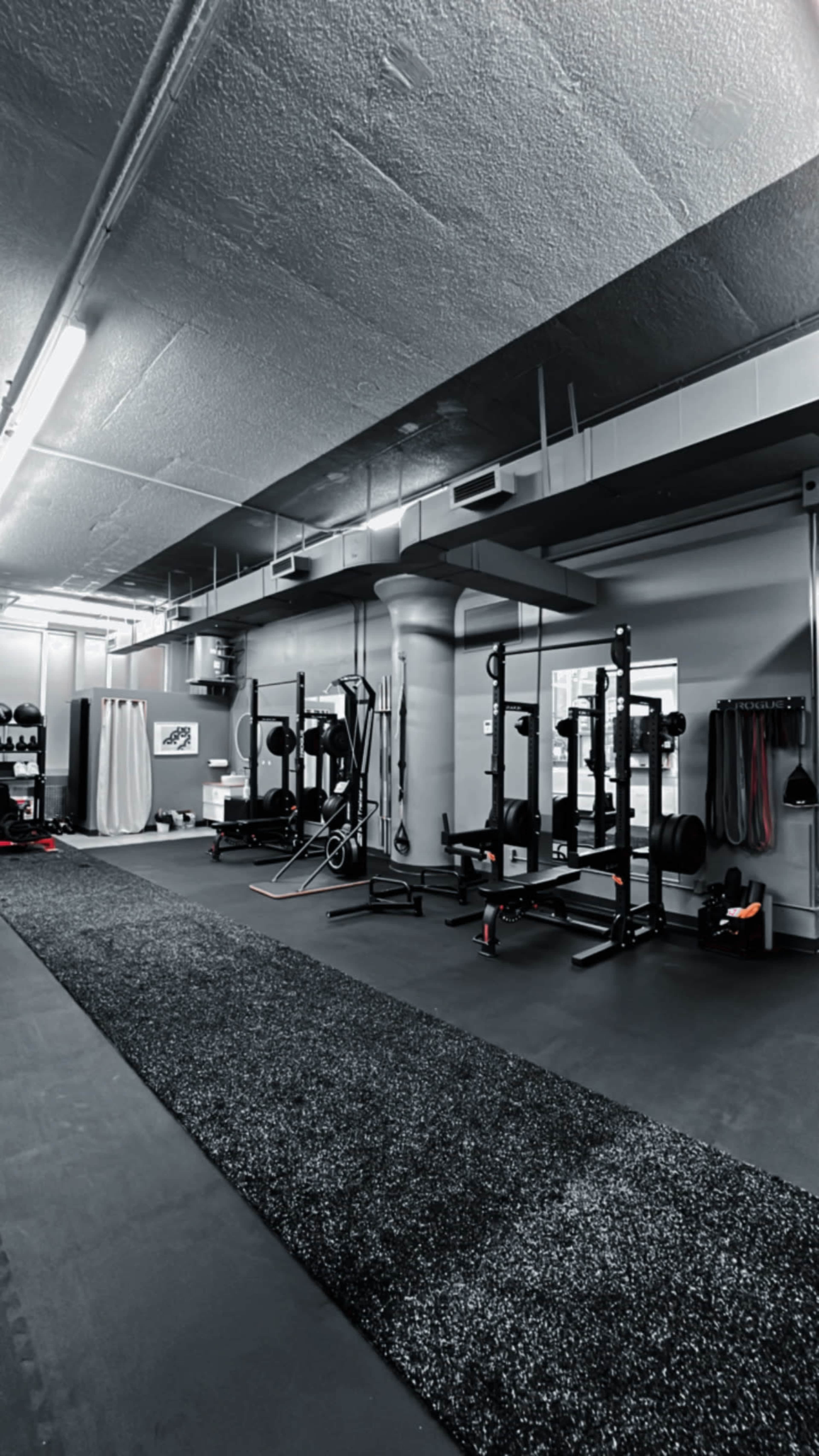 An empty gym interior with various weightlifting equipment arranged along the walls and a rubber flooring surface.