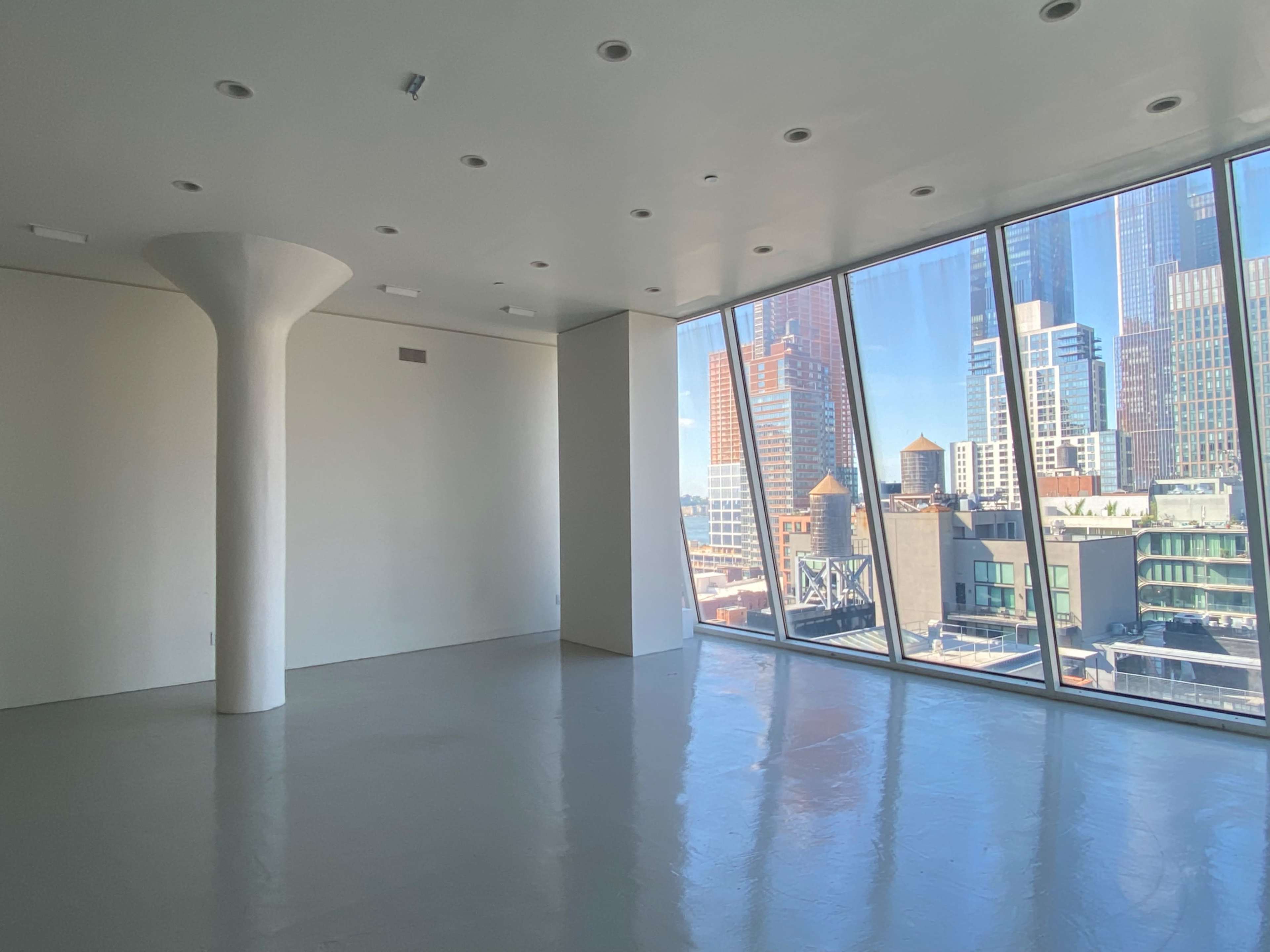 The image shows an empty modern apartment with large floor-to-ceiling windows overlooking a city skyline.