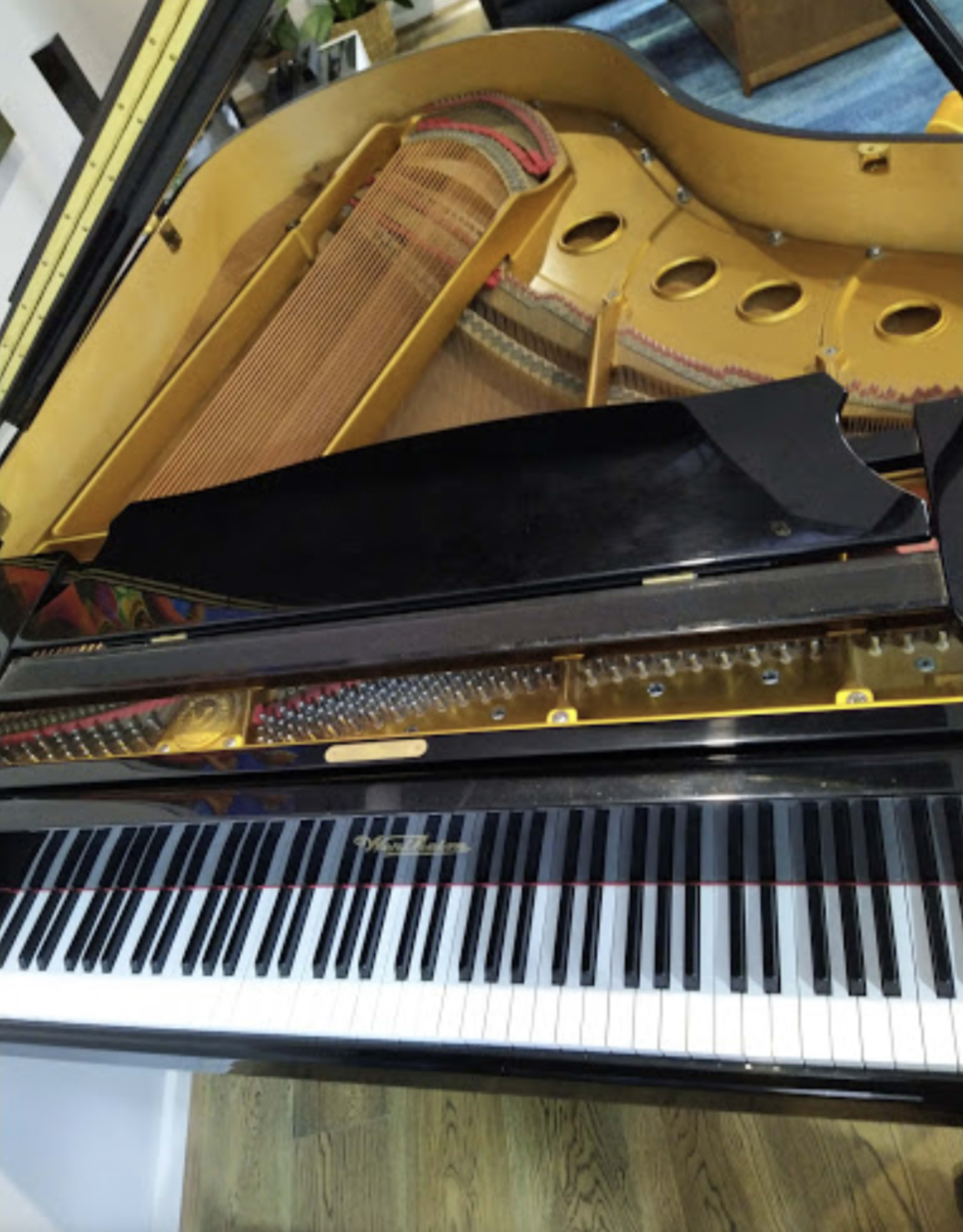 The image shows the top view of a black grand piano with its lid open, revealing the strings and interior features.