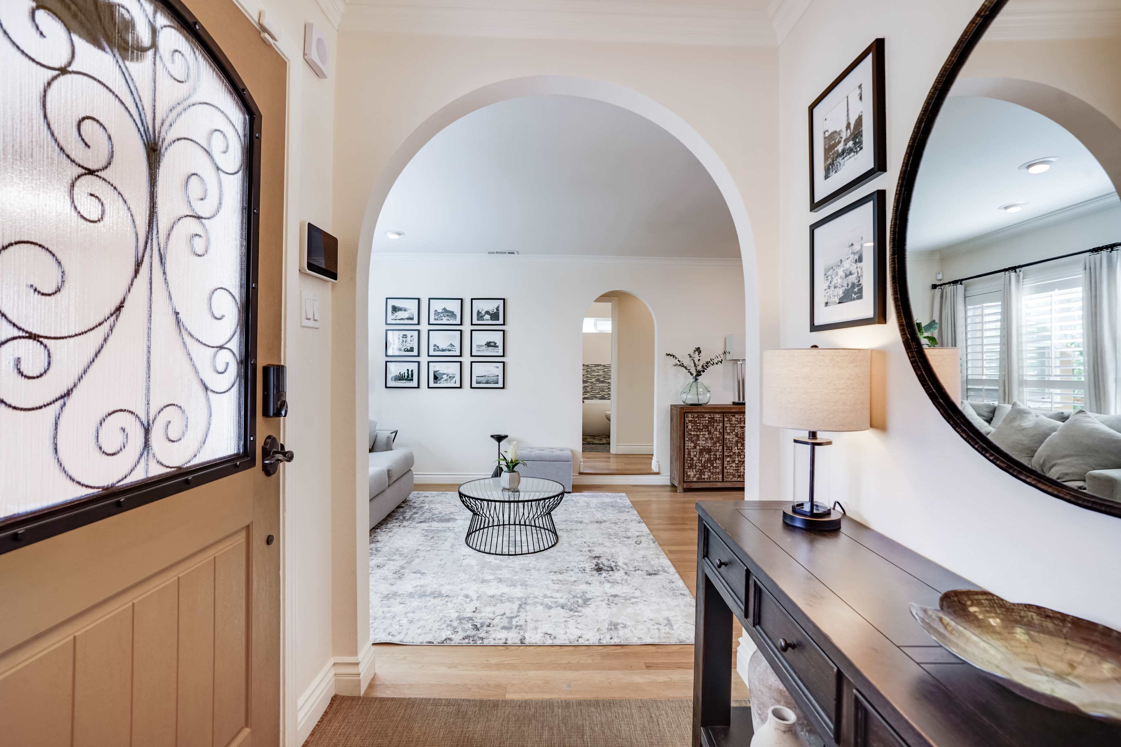 A foyer leading into a living room, featuring an arched entryway, a round mirror, and a coffee table on a rug.
