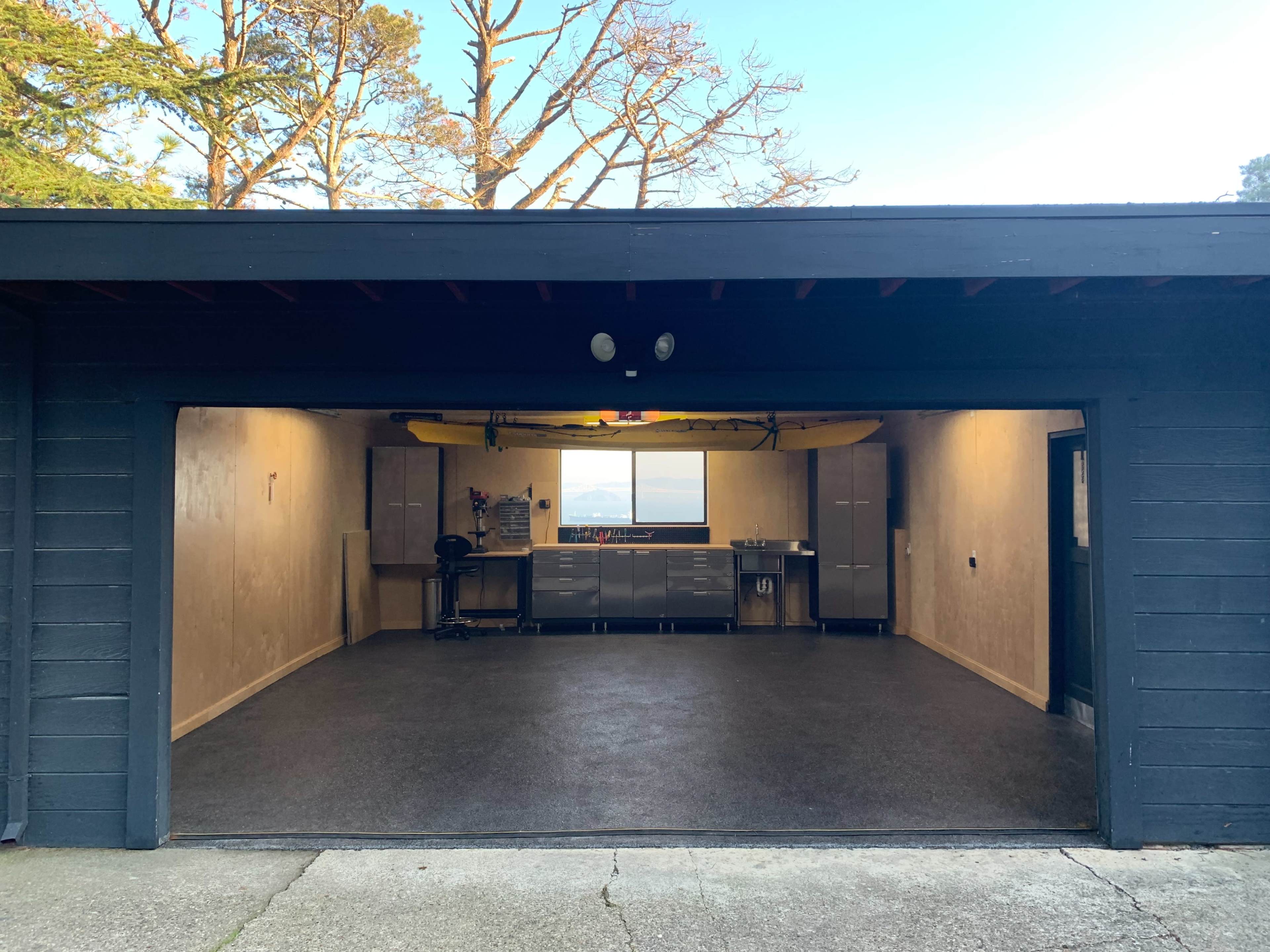 A spacious garage with a workbench and a kayak mounted on the ceiling, illuminated by natural light from a window.