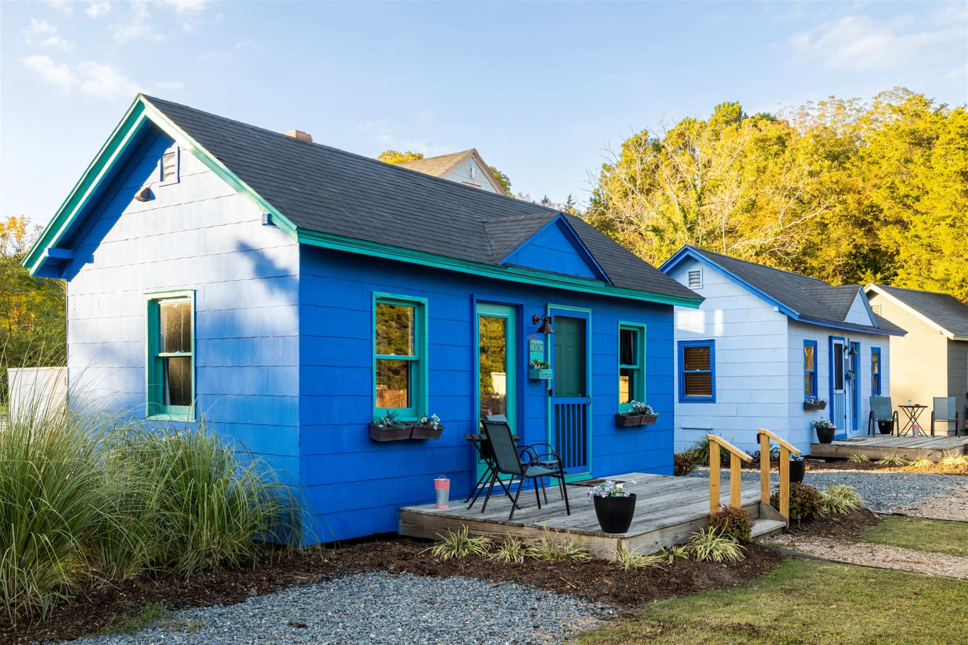 Two brightly colored homes, one blue and one light blue, are situated side by side with a wooden porch and steps in a landscaped setting.