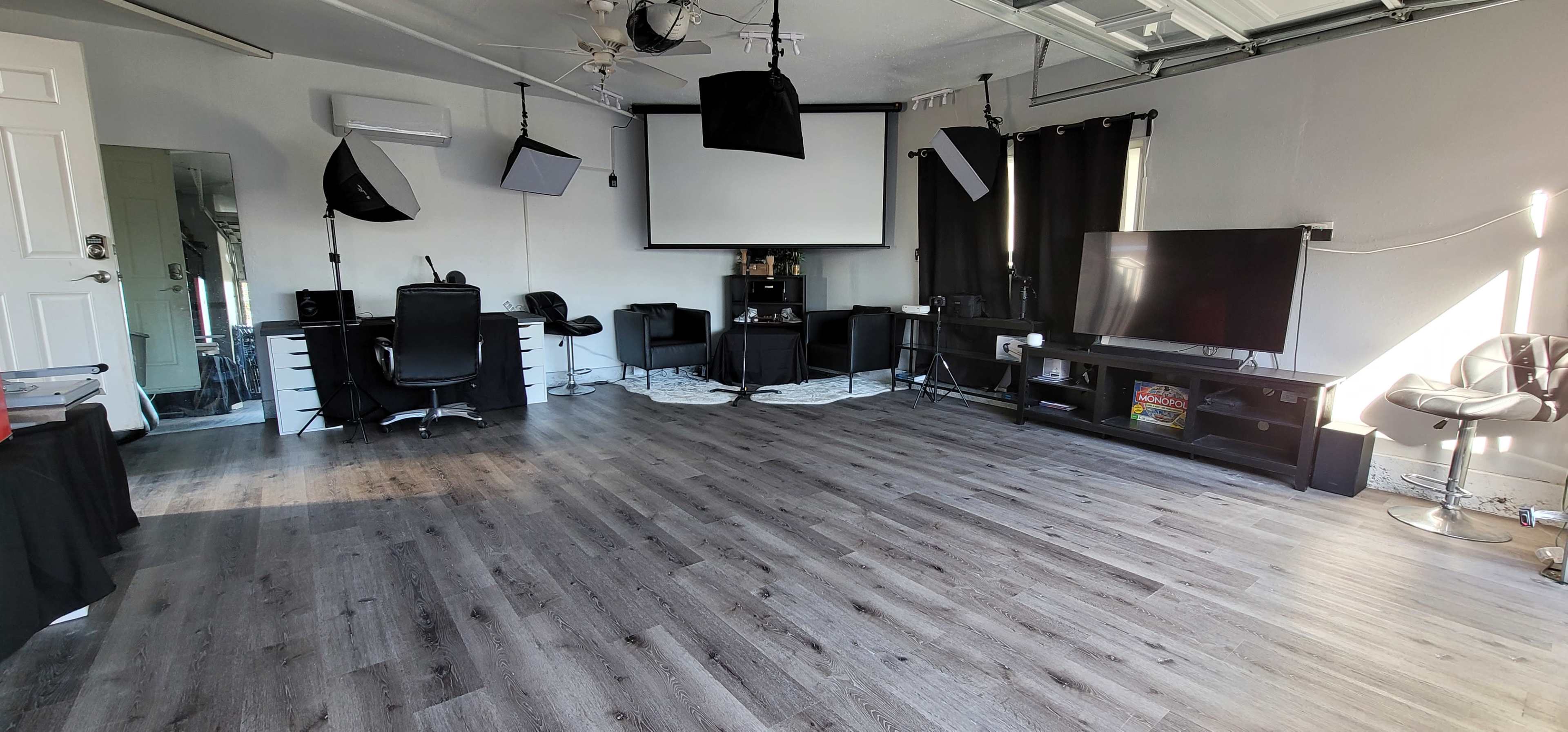 The room features a large, empty space with a smooth floor, equipped with a projection screen, a TV, several black chairs, and softbox lighting setups.