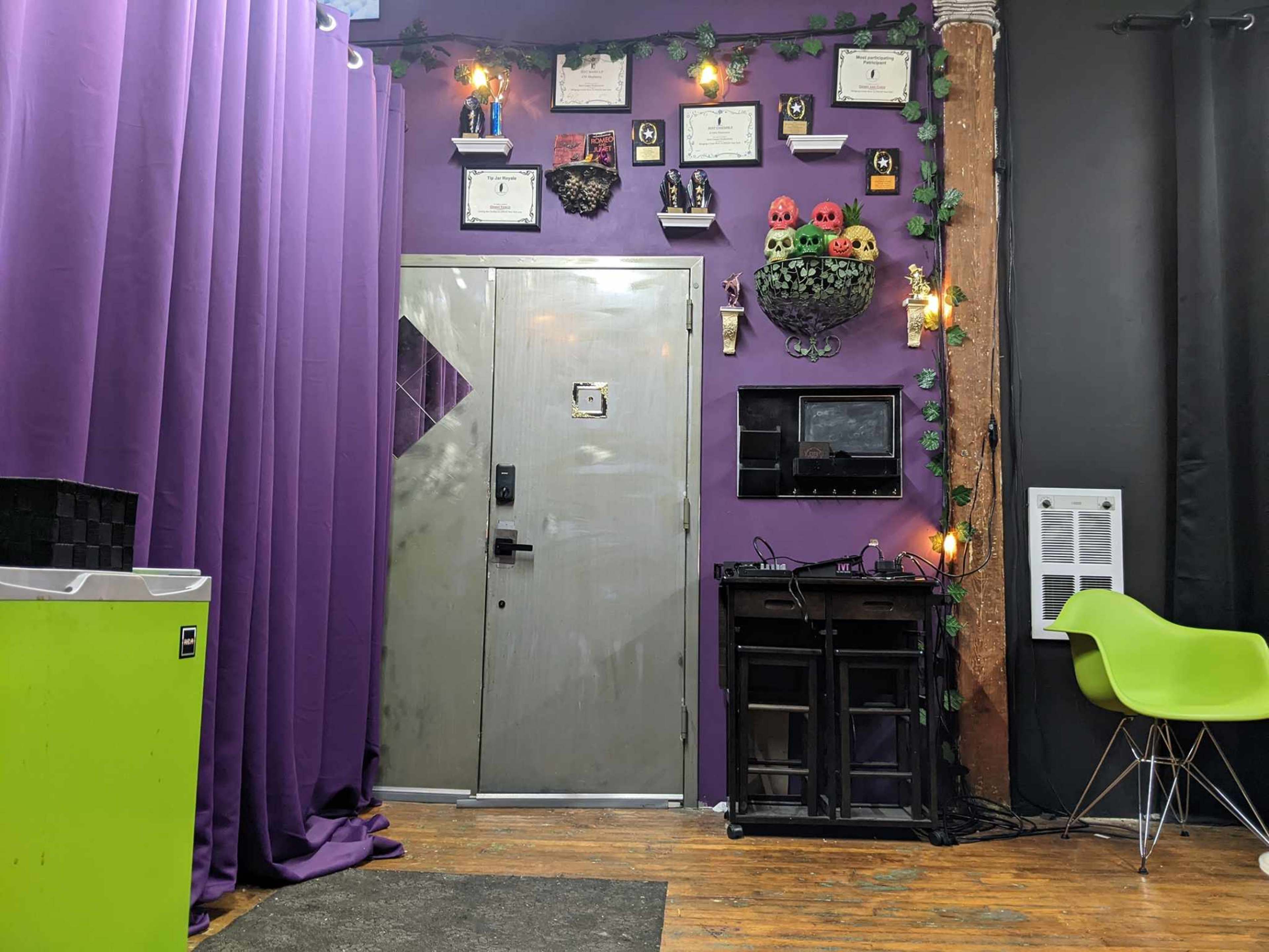 A vibrant purple wall adorned with certificates, a gray door, and a small black table with electronic equipment.