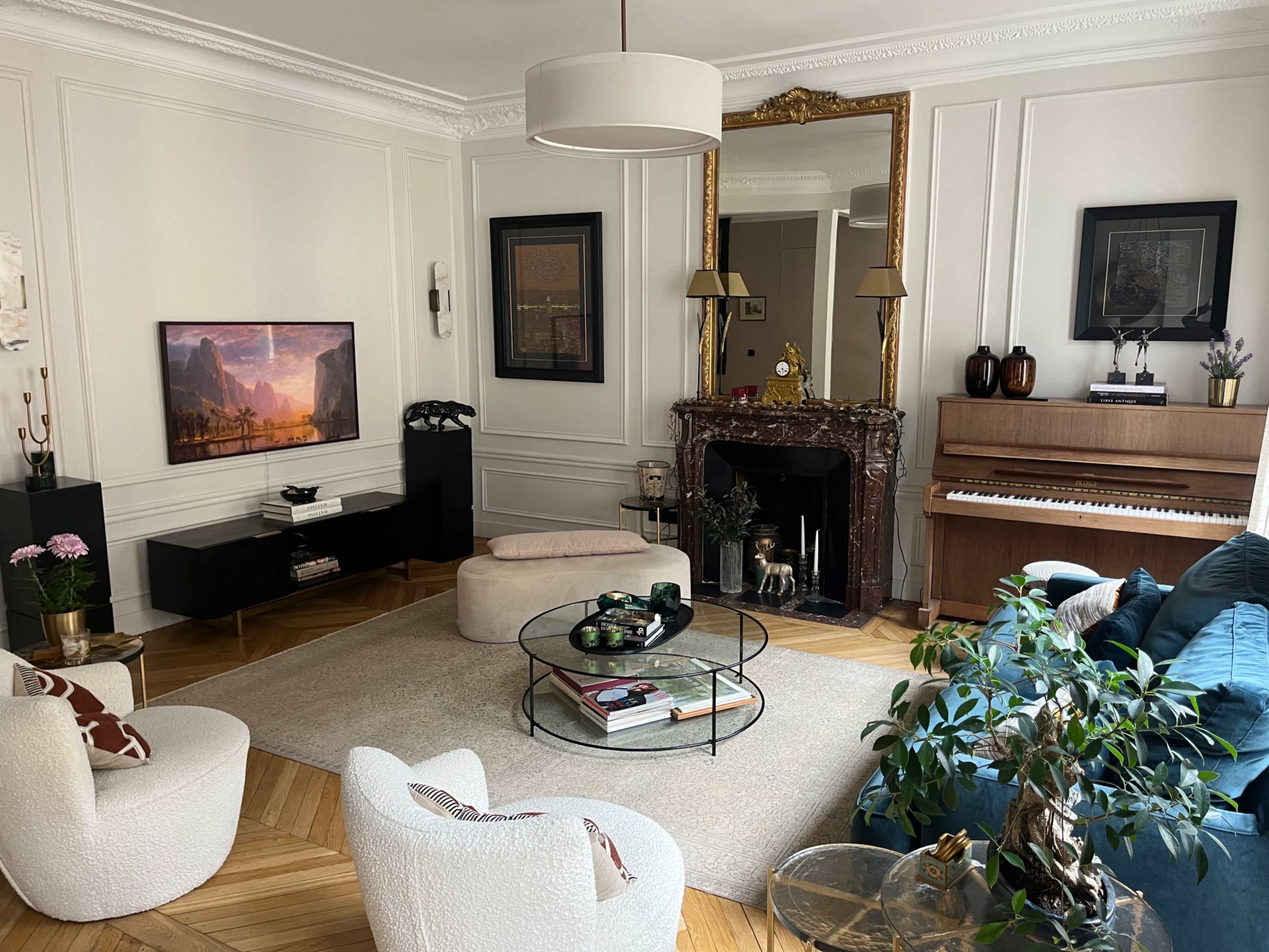 A well-furnished living room features a television, a piano, stylish seating, and decorative plants, all arranged around a central coffee table.