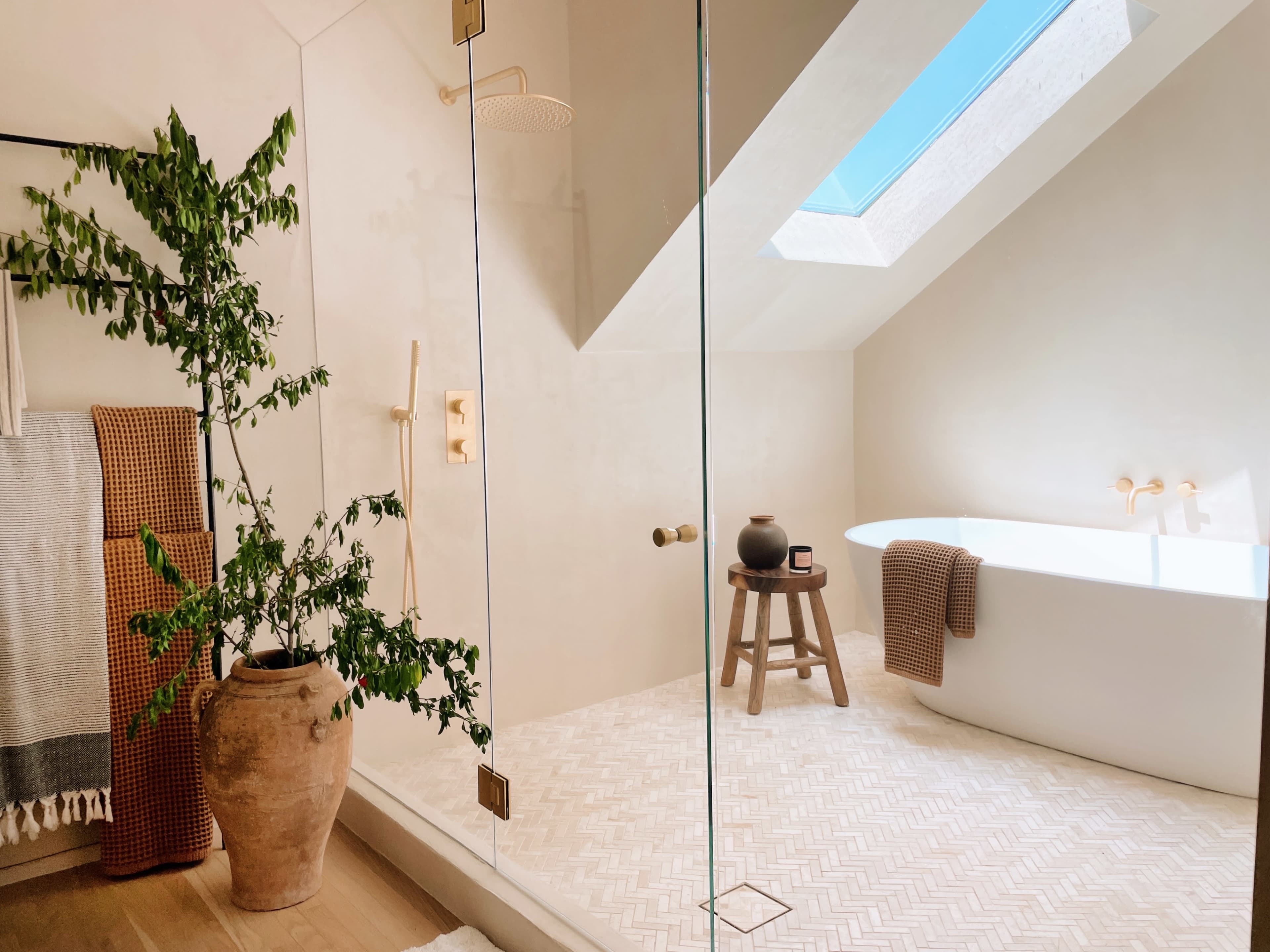 A modern bathroom featuring a glass shower enclosure, a freestanding bathtub, and a potted plant beside a wooden stool.