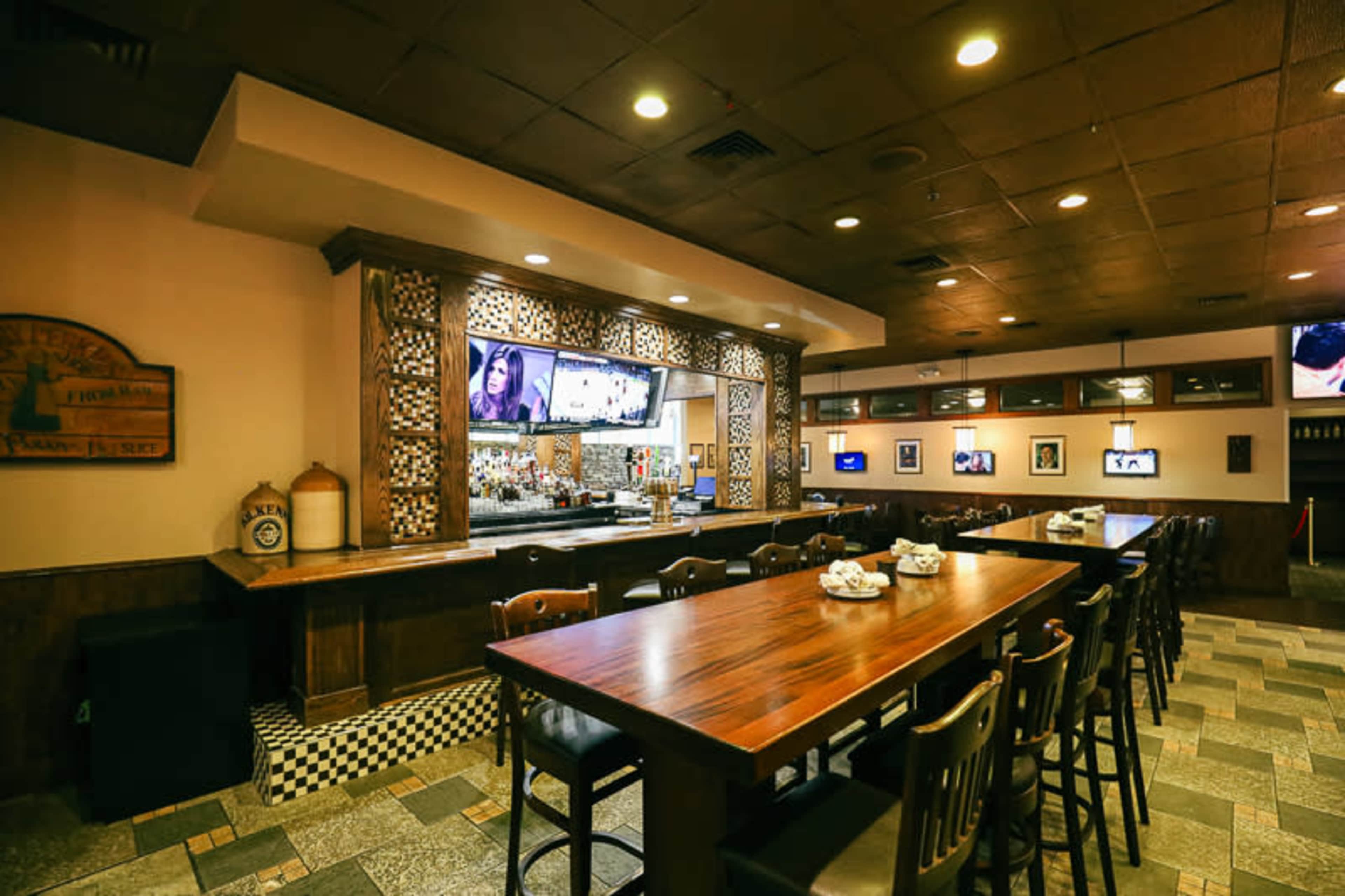 A restaurant interior with a long wooden bar and seating area, featuring a decorative bar counter and multiple televisions on the walls.