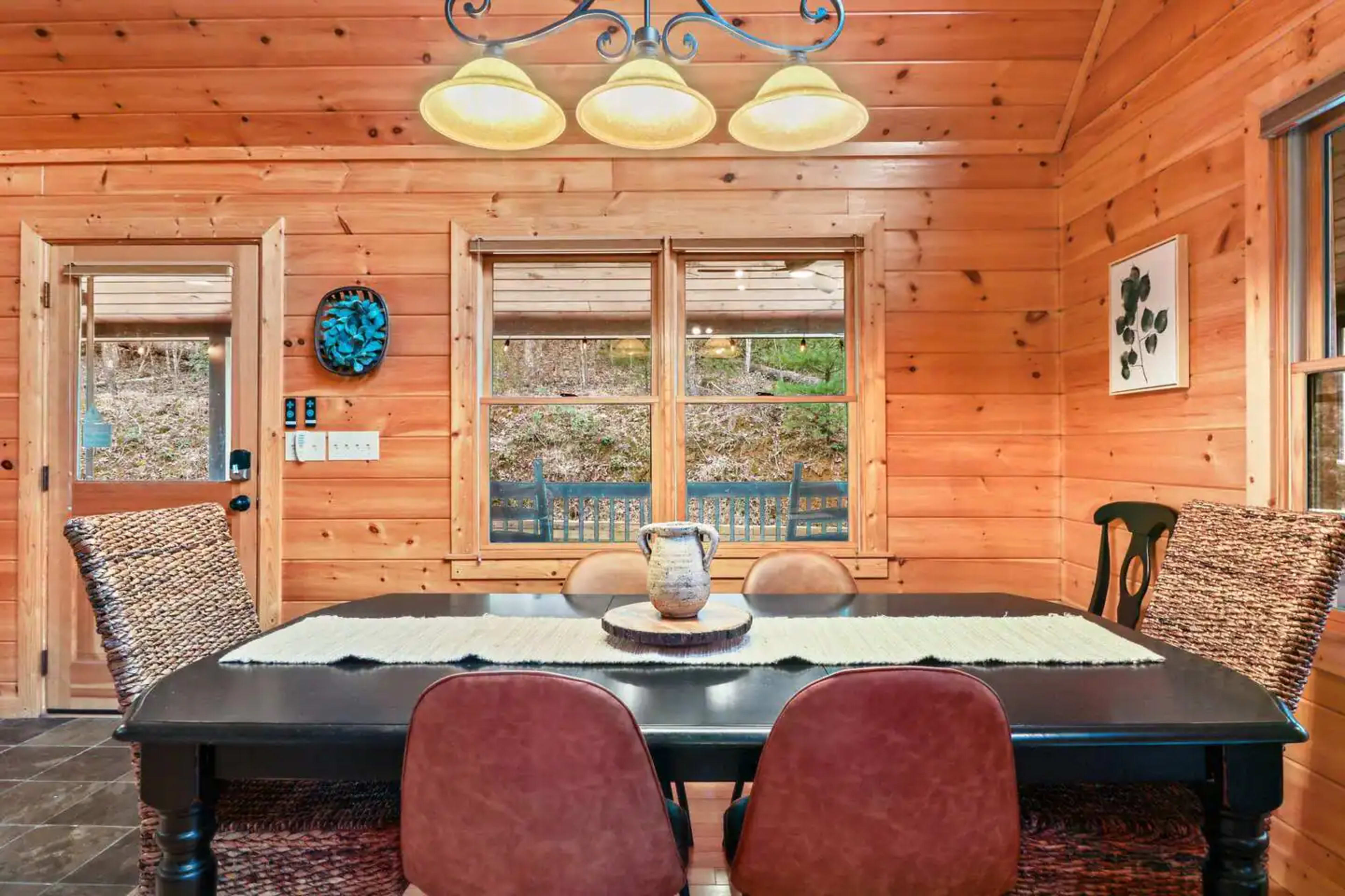 A wooden dining area with a black table, brown chairs, and a light fixture hanging above.