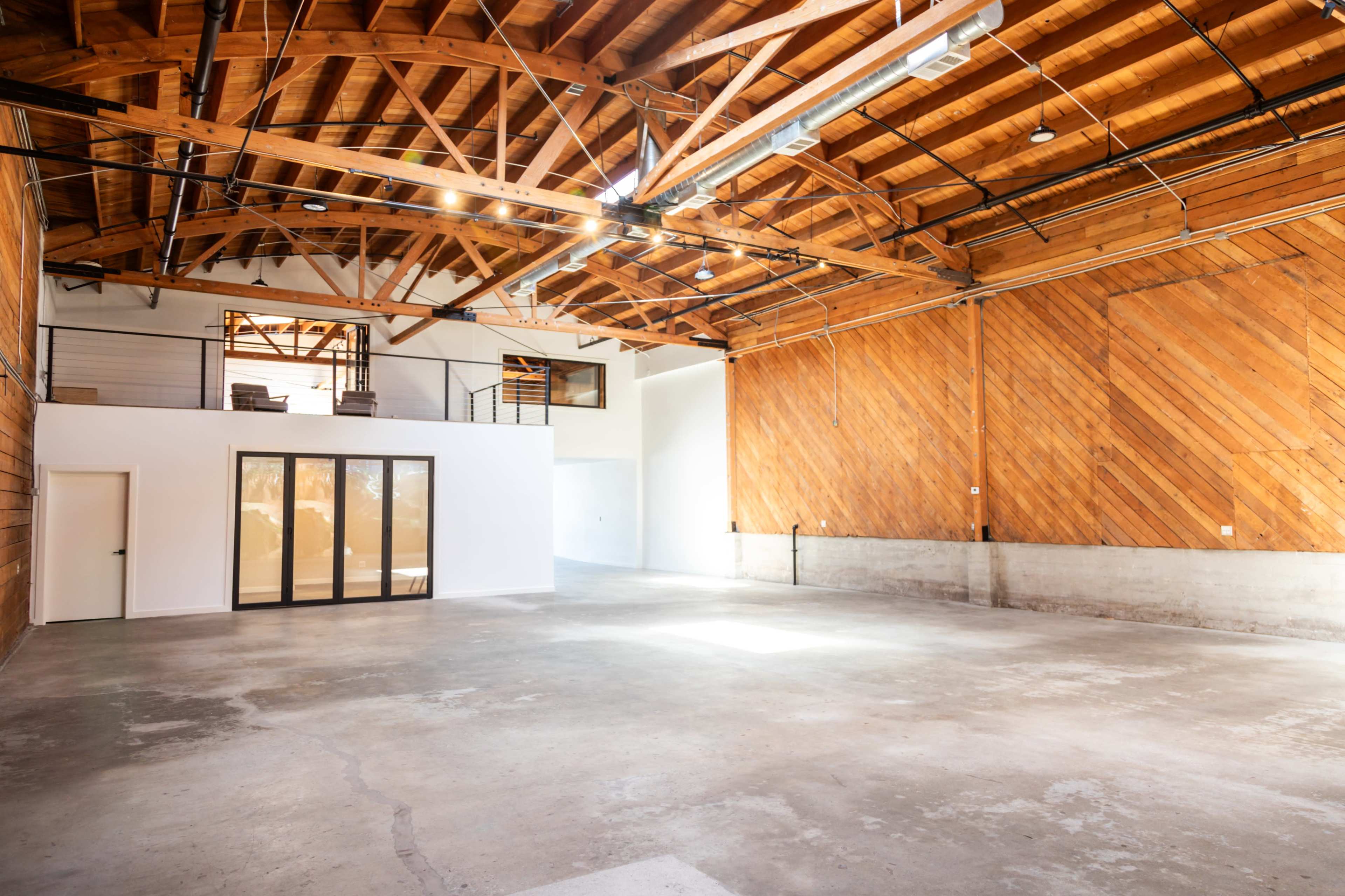 A spacious, empty industrial-style room with wooden beams and a concrete floor.