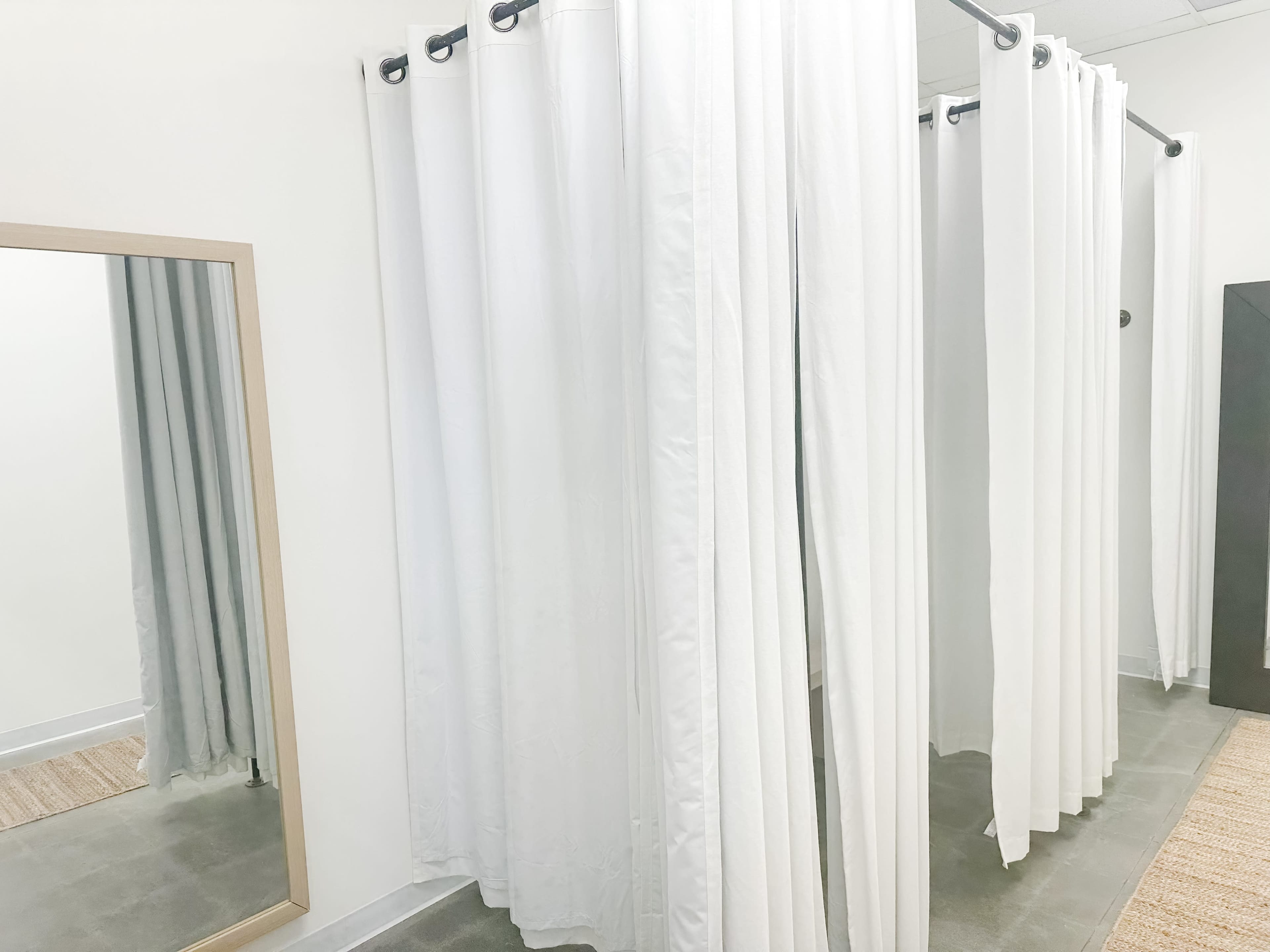 A fitting room area with white curtains, a large mirror, and a gray floor.