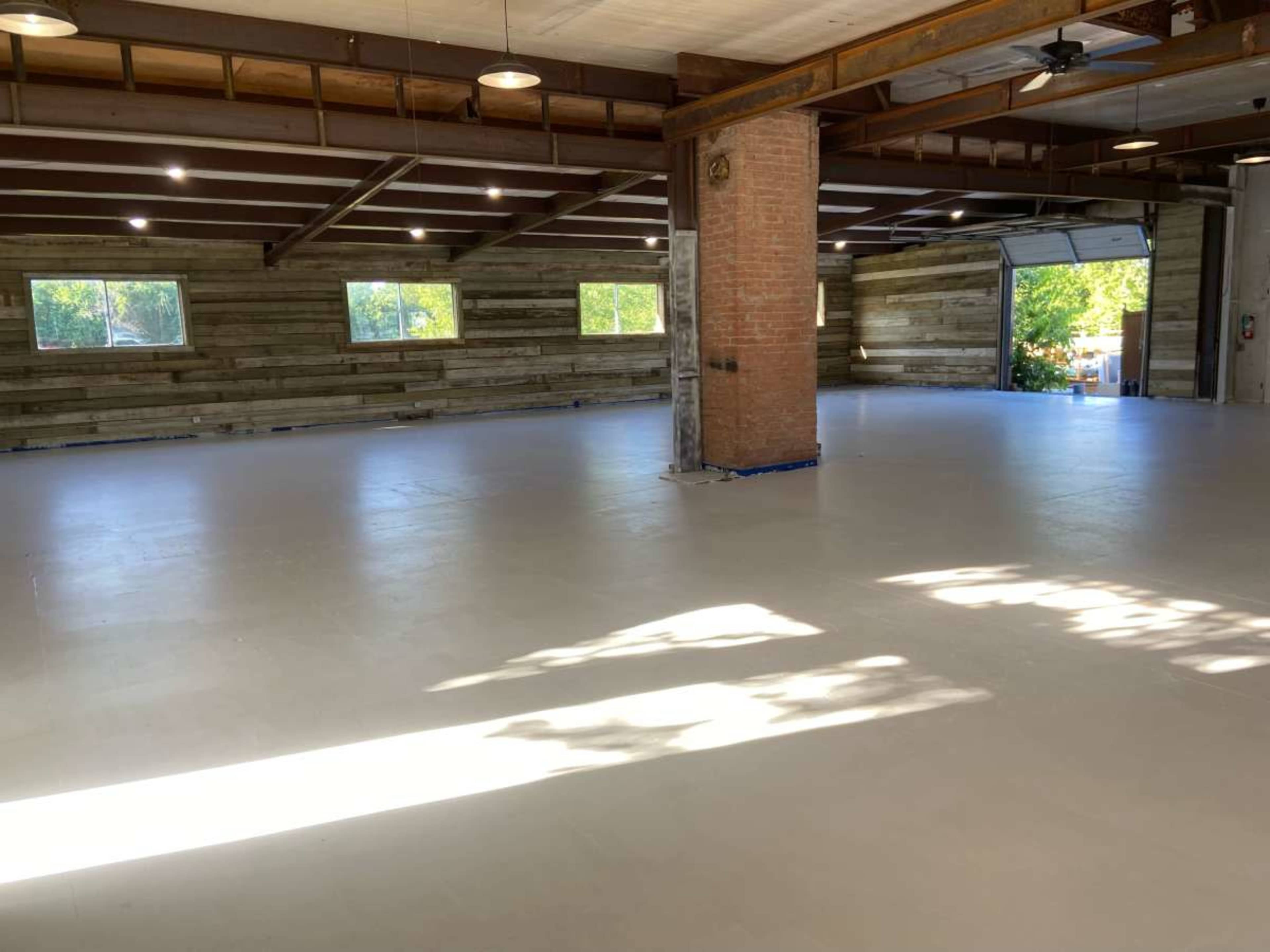 An empty industrial space with a polished concrete floor, large windows, and wooden walls.