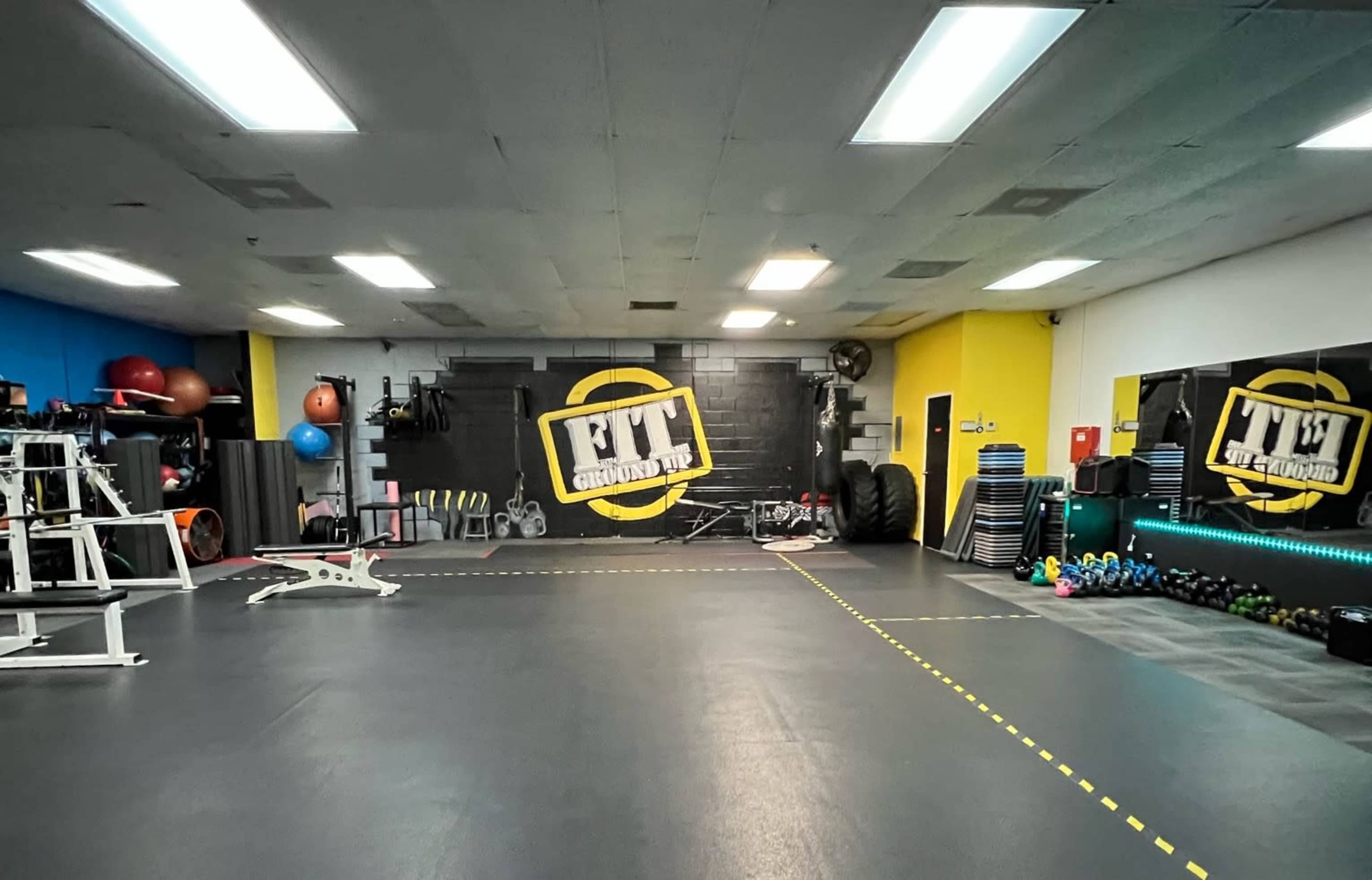 An empty gym interior with exercise equipment, weights, and fitness accessories organized along the walls.
