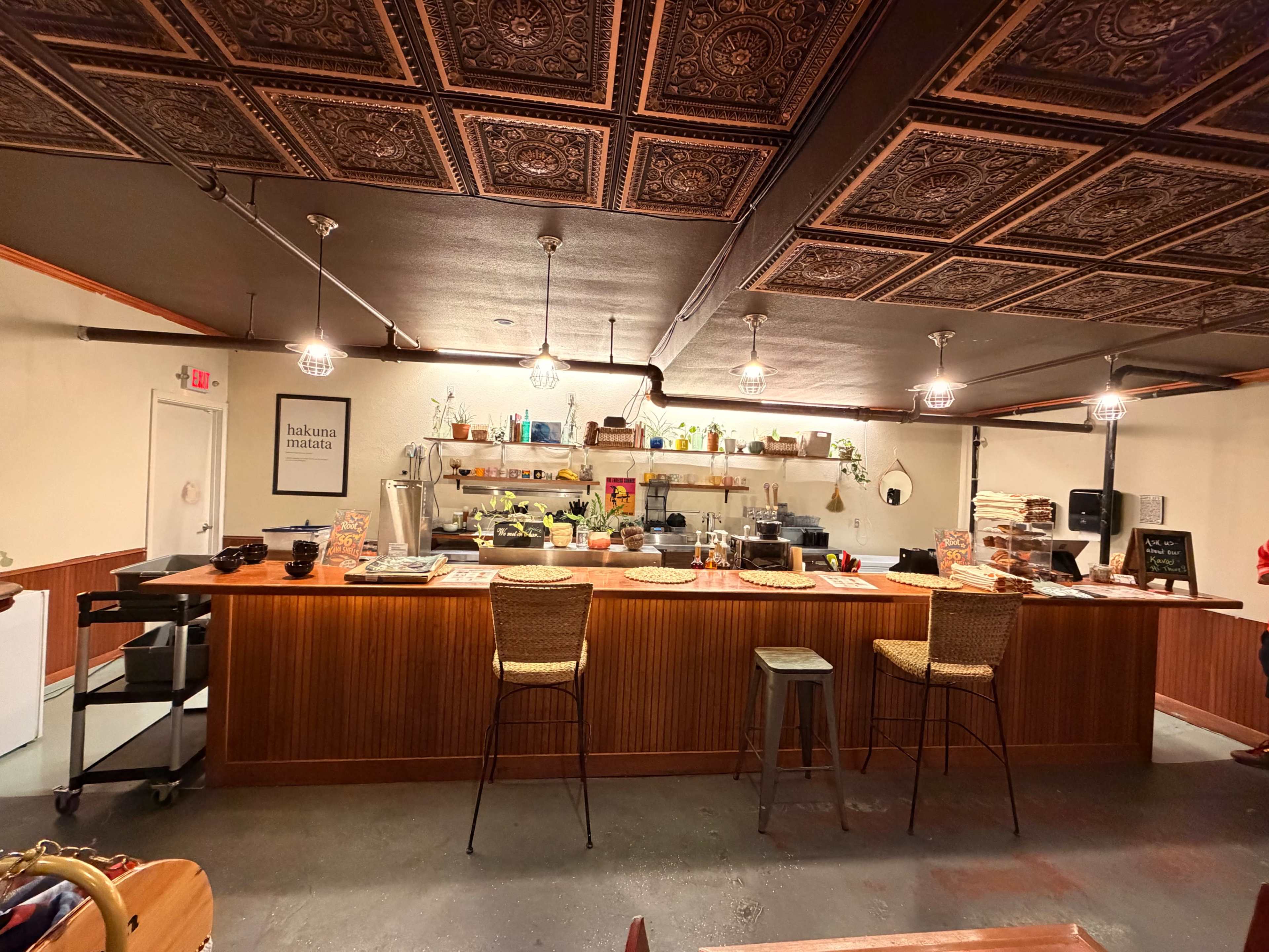 The image shows a cozy coffee shop interior with a wooden counter, bar stools, and a variety of items displayed on shelves.