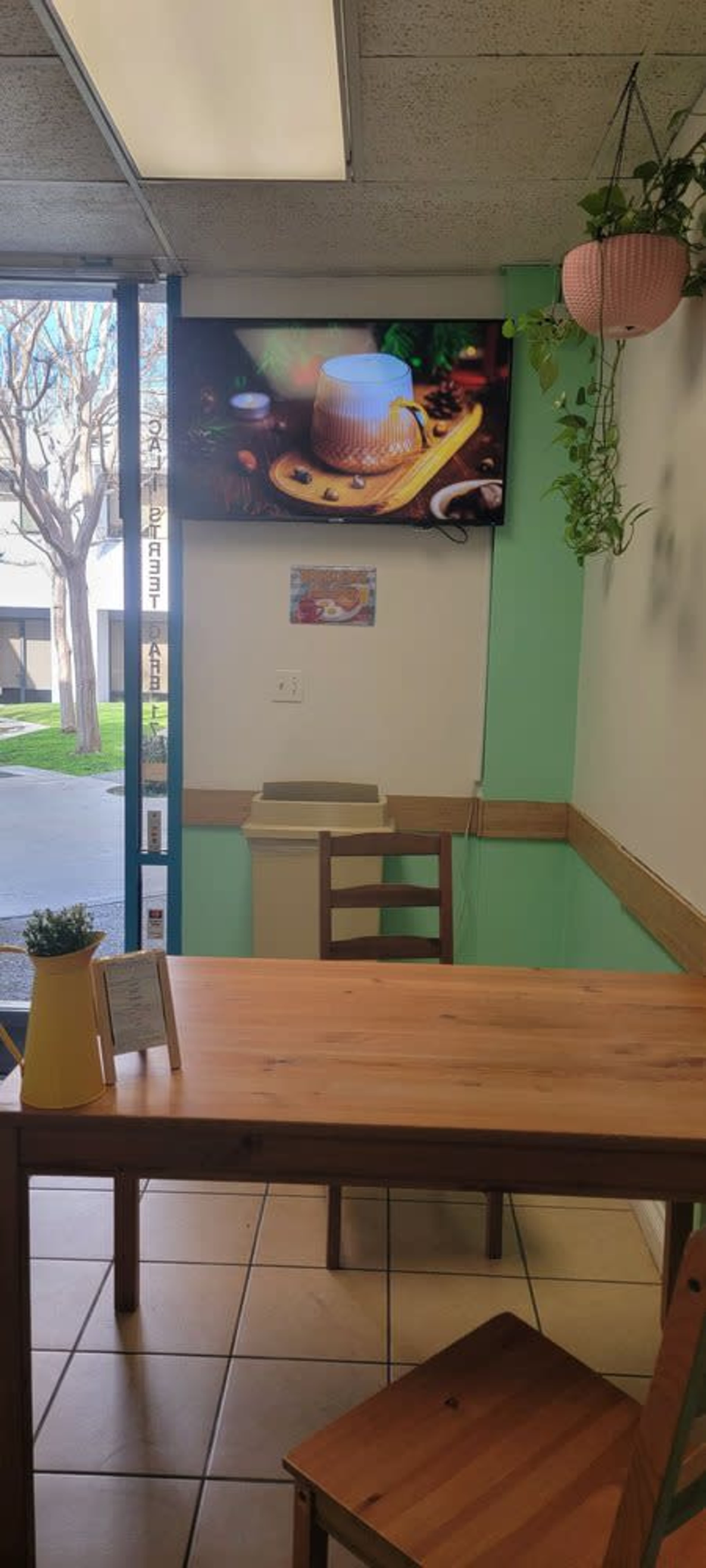 A wooden table and two chairs are set up in a small dining area with a large television mounted on the wall displaying an image of a mug.