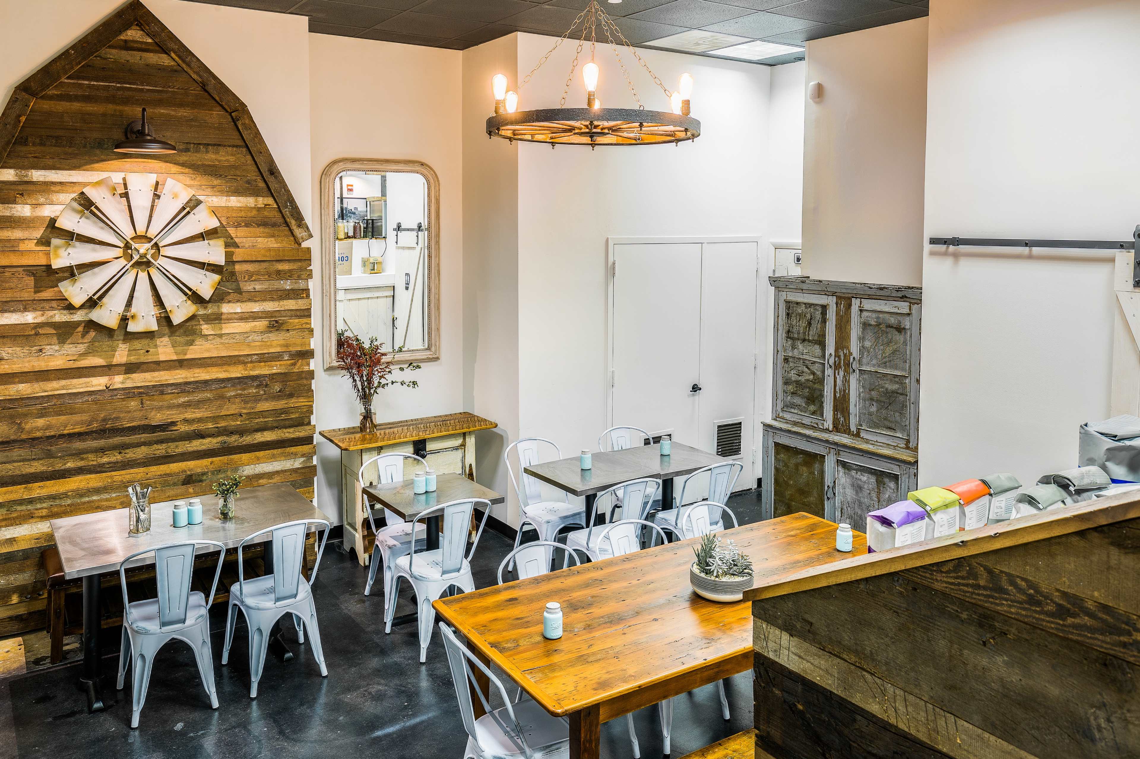 A modern café interior with wooden walls, metal chairs, and multiple tables arranged in a spacious layout.