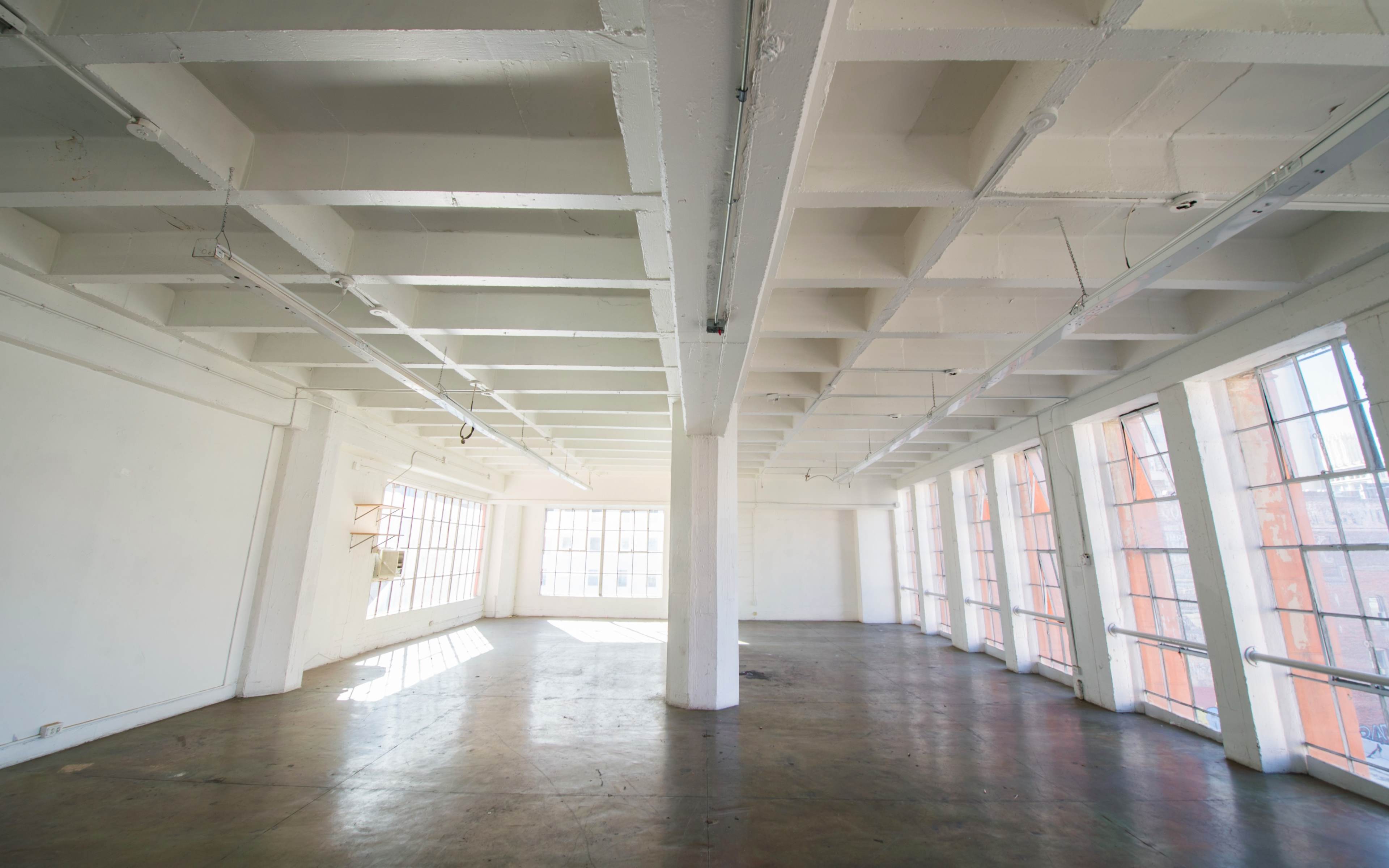 A large, empty room with high ceilings, white walls, and ample natural light from large windows.