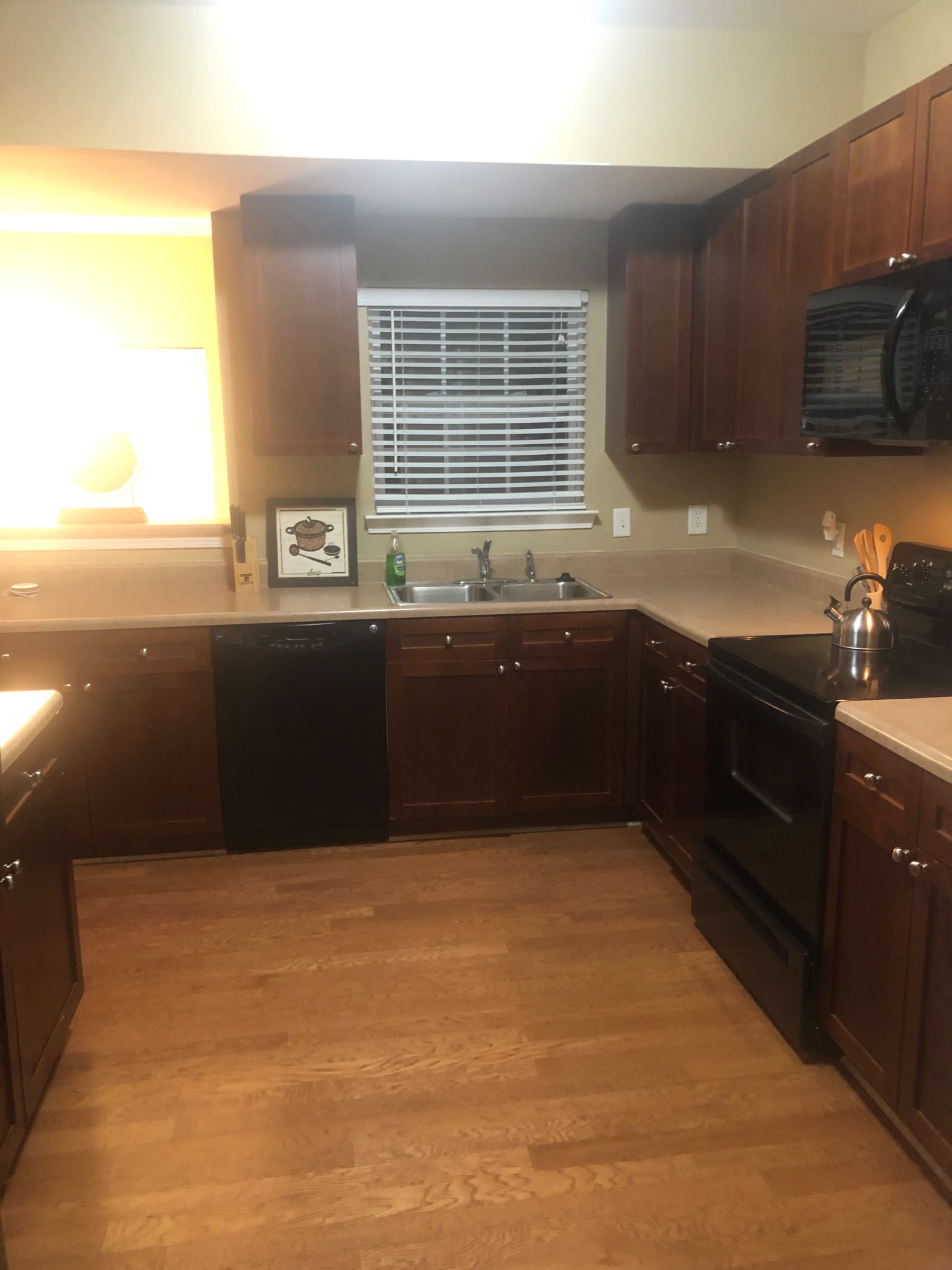 A kitchen with wooden cabinets, a black dishwasher, and an oven, featuring a window with blinds and a counter with kitchen utensils.