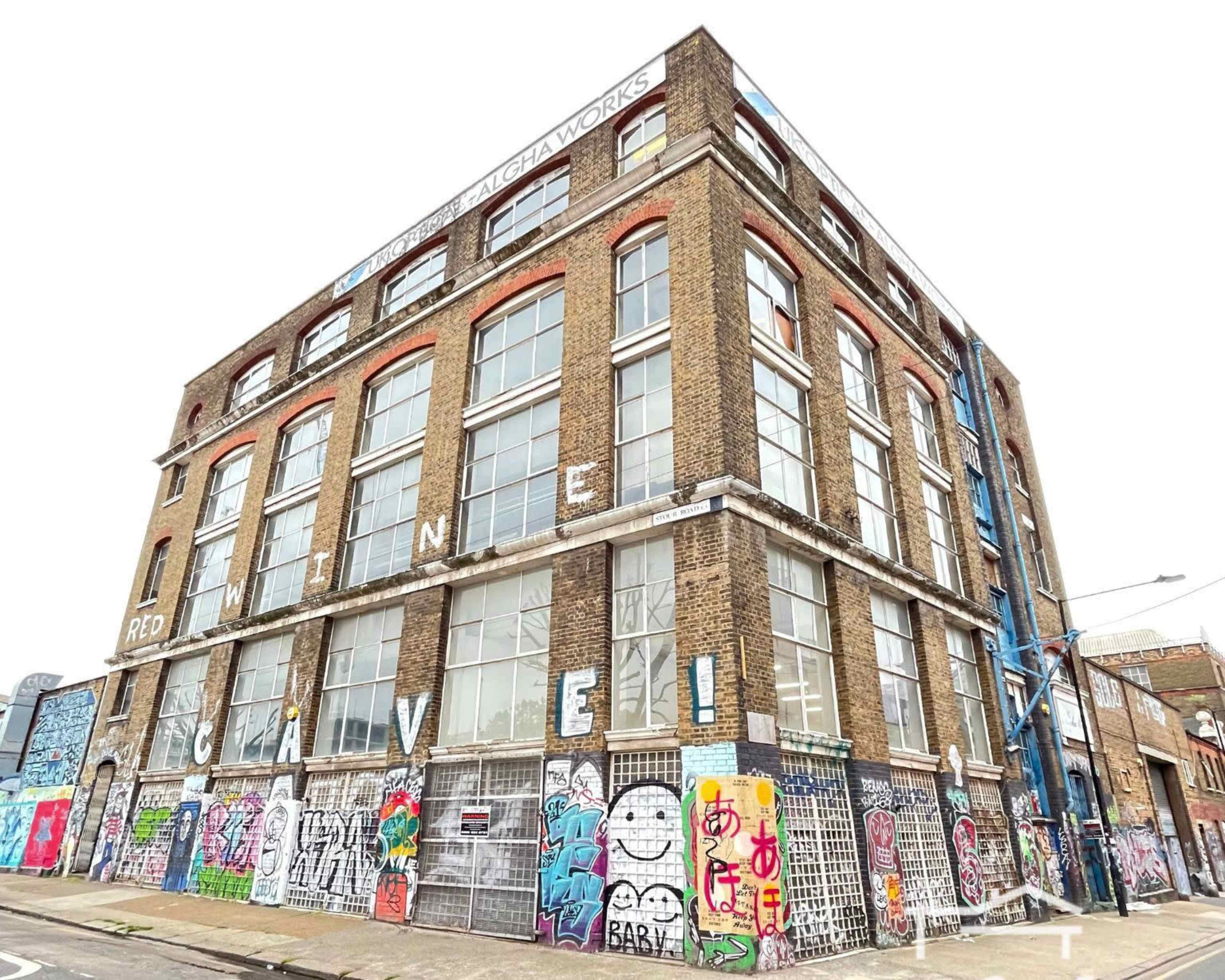 A large, brick building with multiple floors is covered in colorful graffiti and features several windows and metal grates.