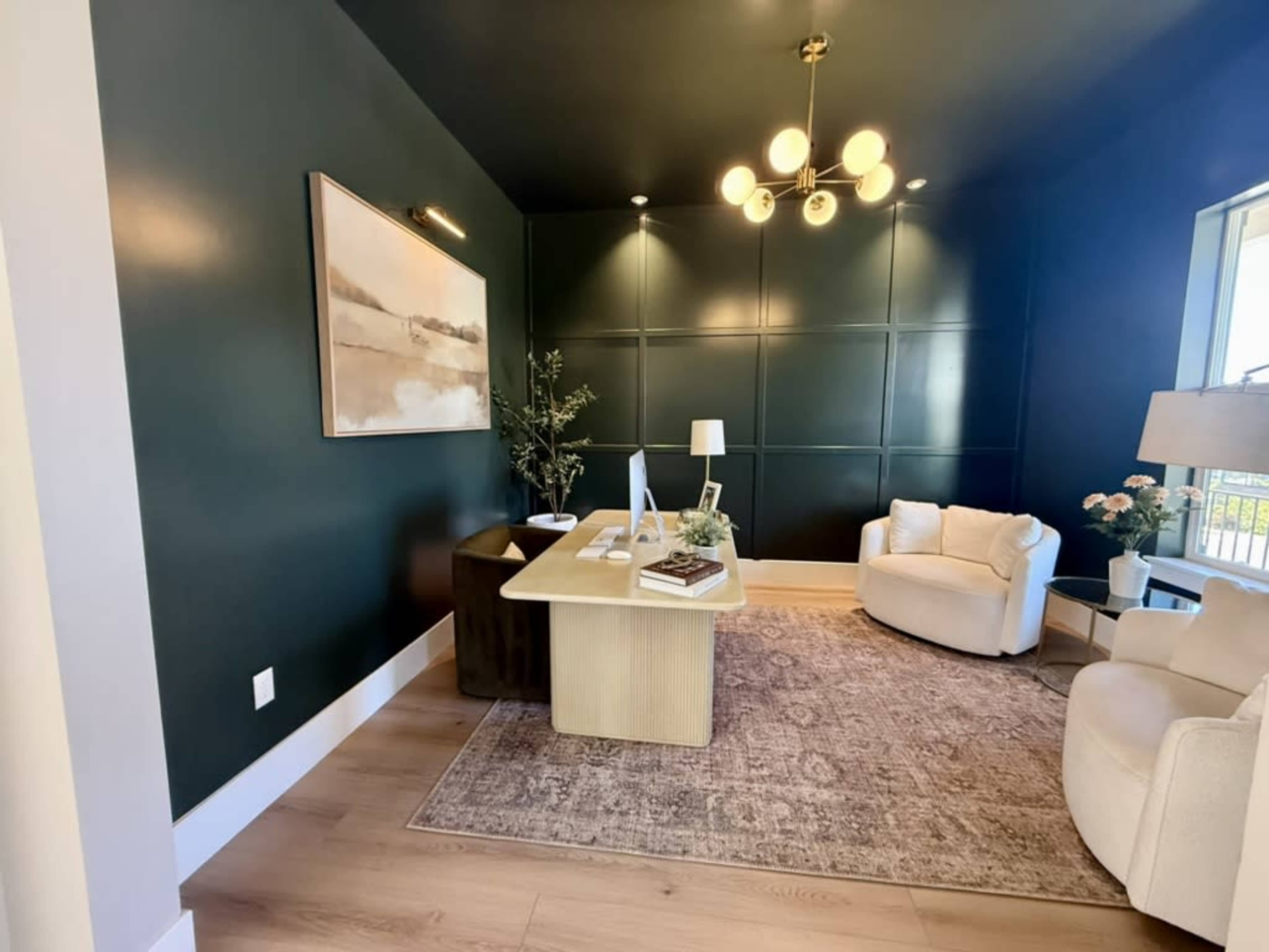 The image depicts a modern office space featuring a dark green accent wall, a light-colored desk, a comfortable armchair, and decorative elements like a lamp and artwork.