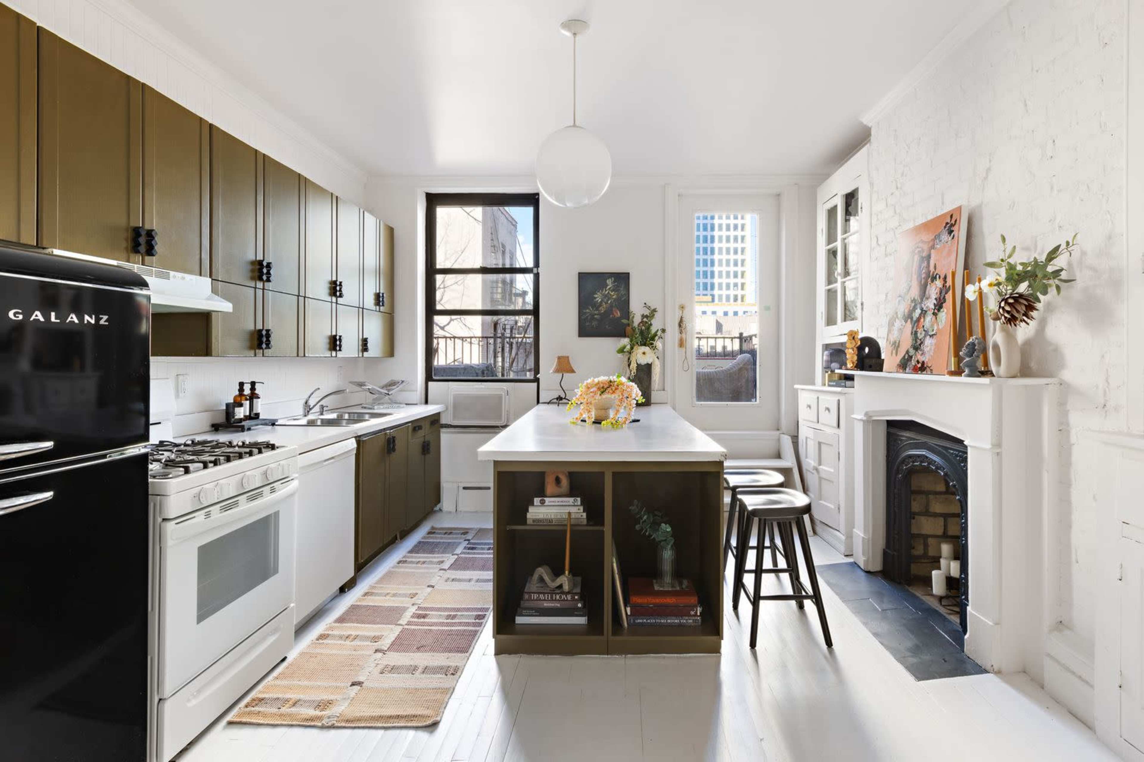 The image shows a modern kitchen featuring a black refrigerator, a white countertop island with bar stools, and a mix of green and white cabinetry.