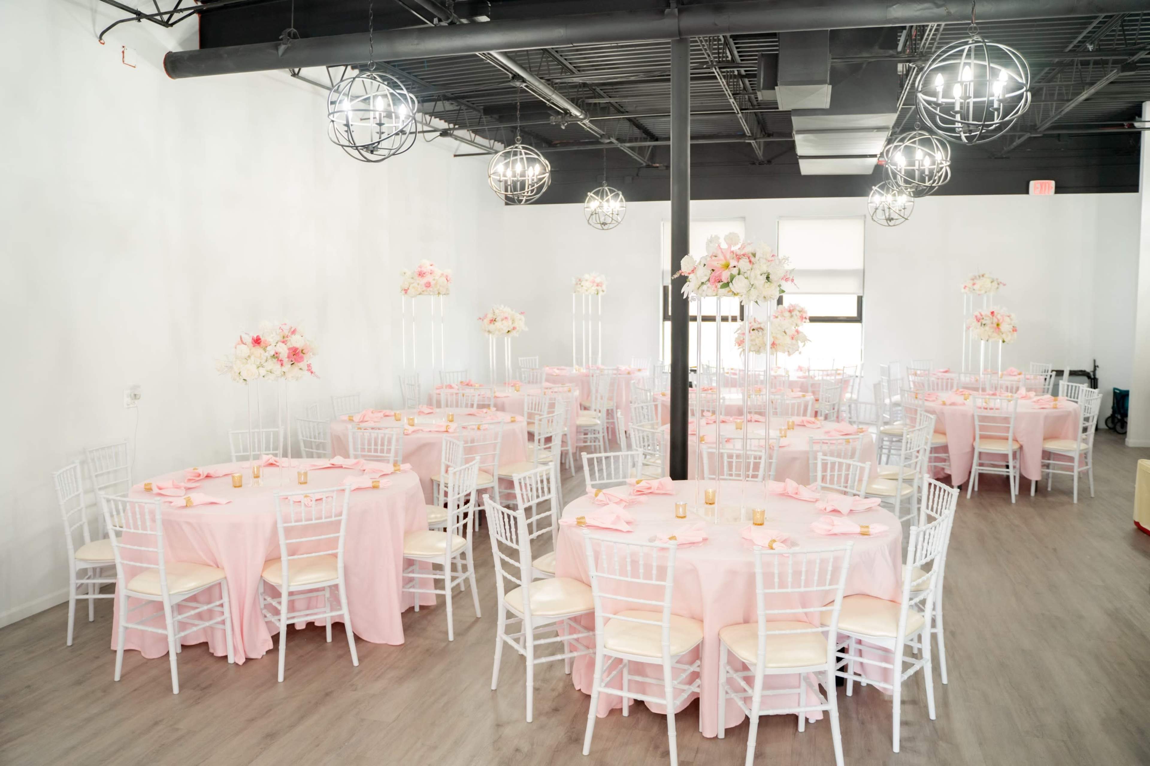 A spacious, elegantly arranged event hall with several round tables covered in pink tablecloths and adorned with floral centerpieces.