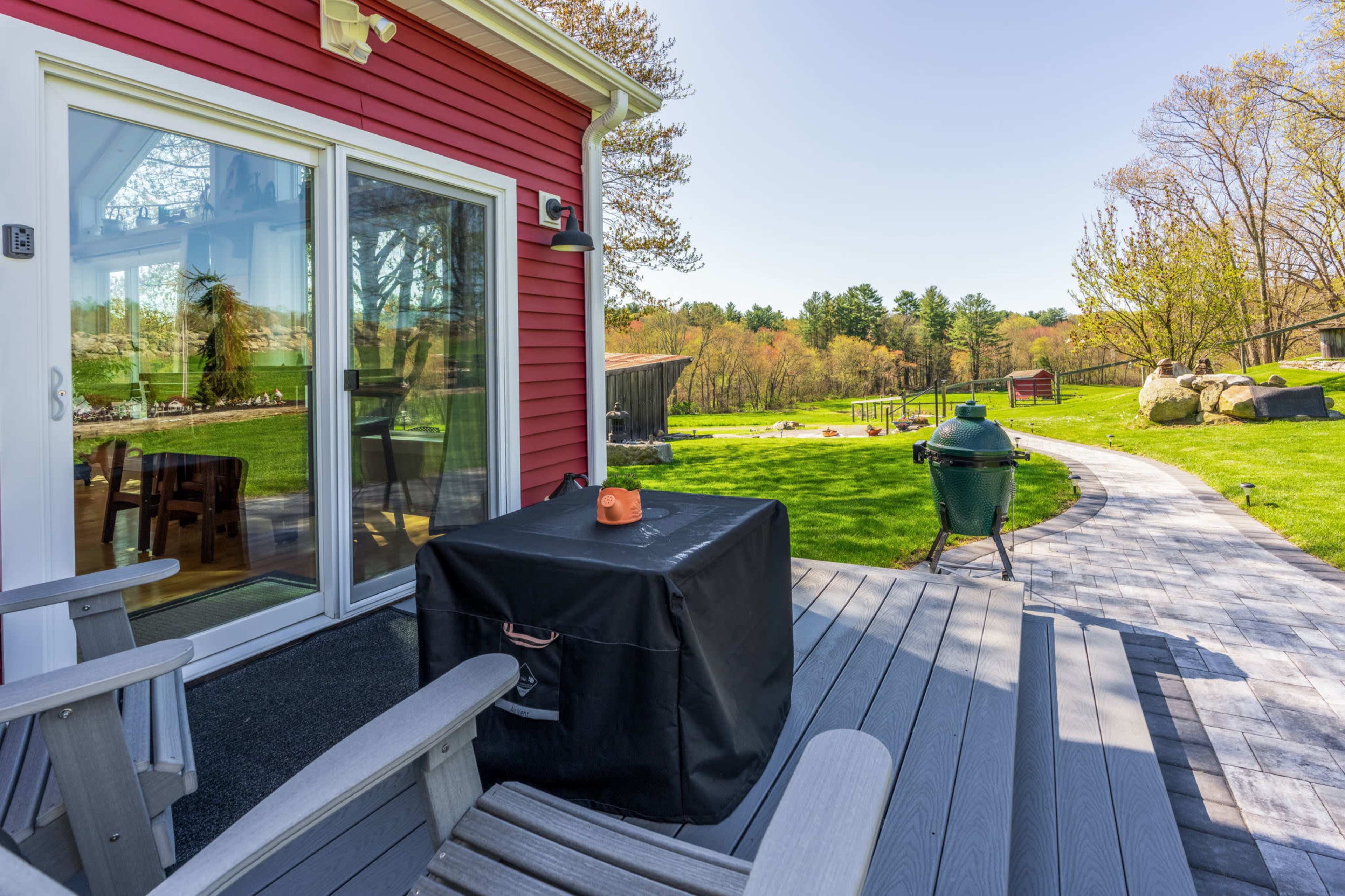 A red house with a patio featuring outdoor furniture and a grill, set in a green yard with trees and a winding path.