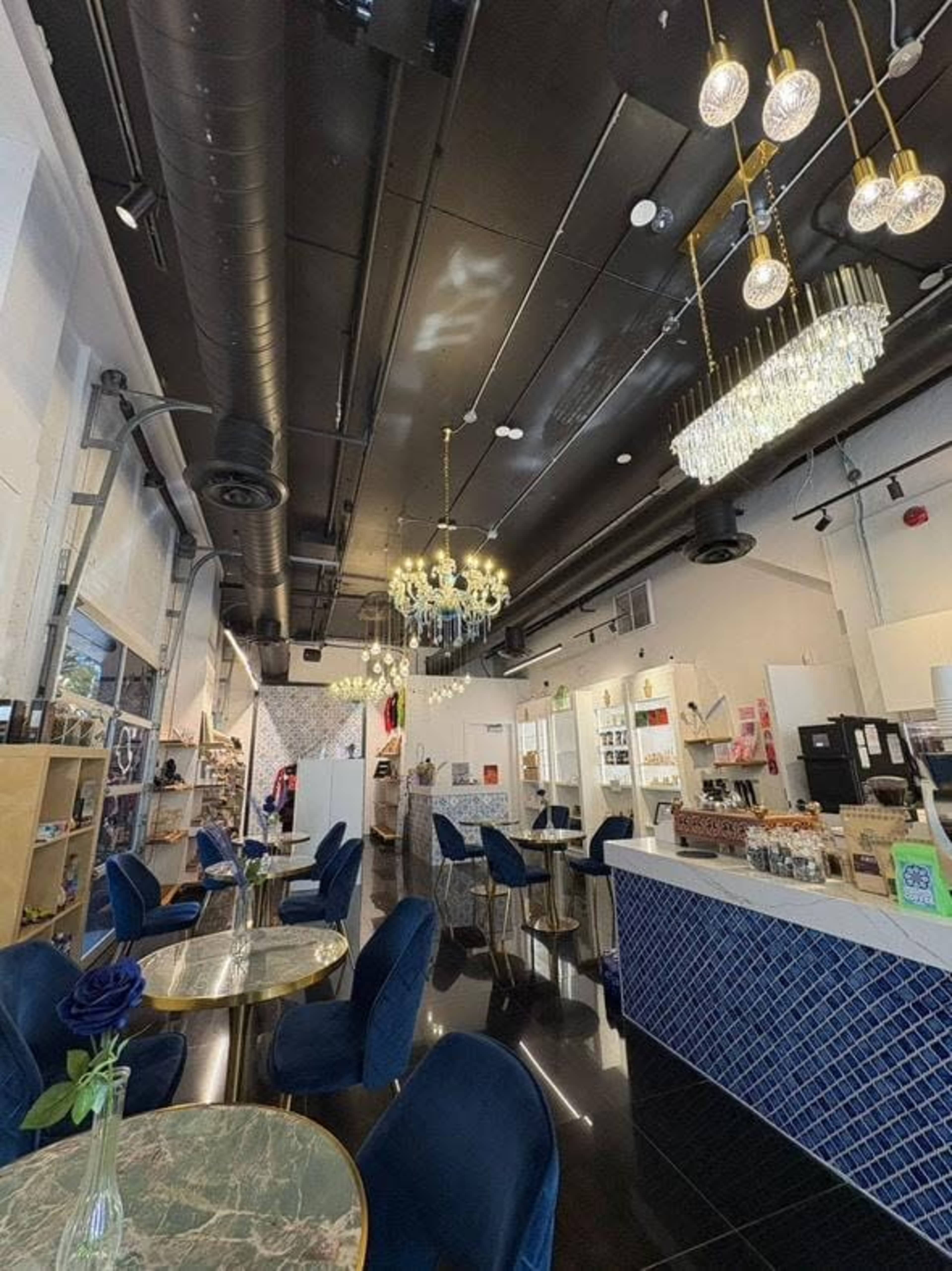 The image shows a modern cafe interior with elegant lighting, blue velvet chairs, and marble-top tables.