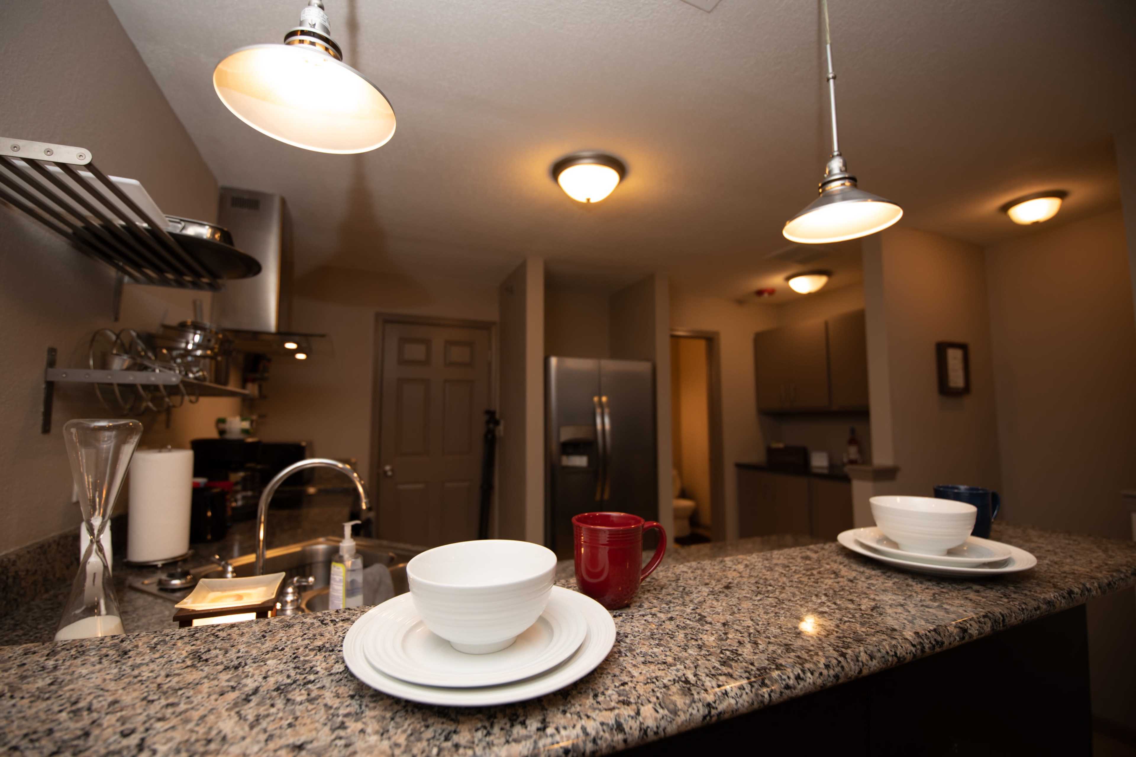 A modern kitchen with granite countertops, two empty bowls on white plates, a red mug, and stainless steel appliances.