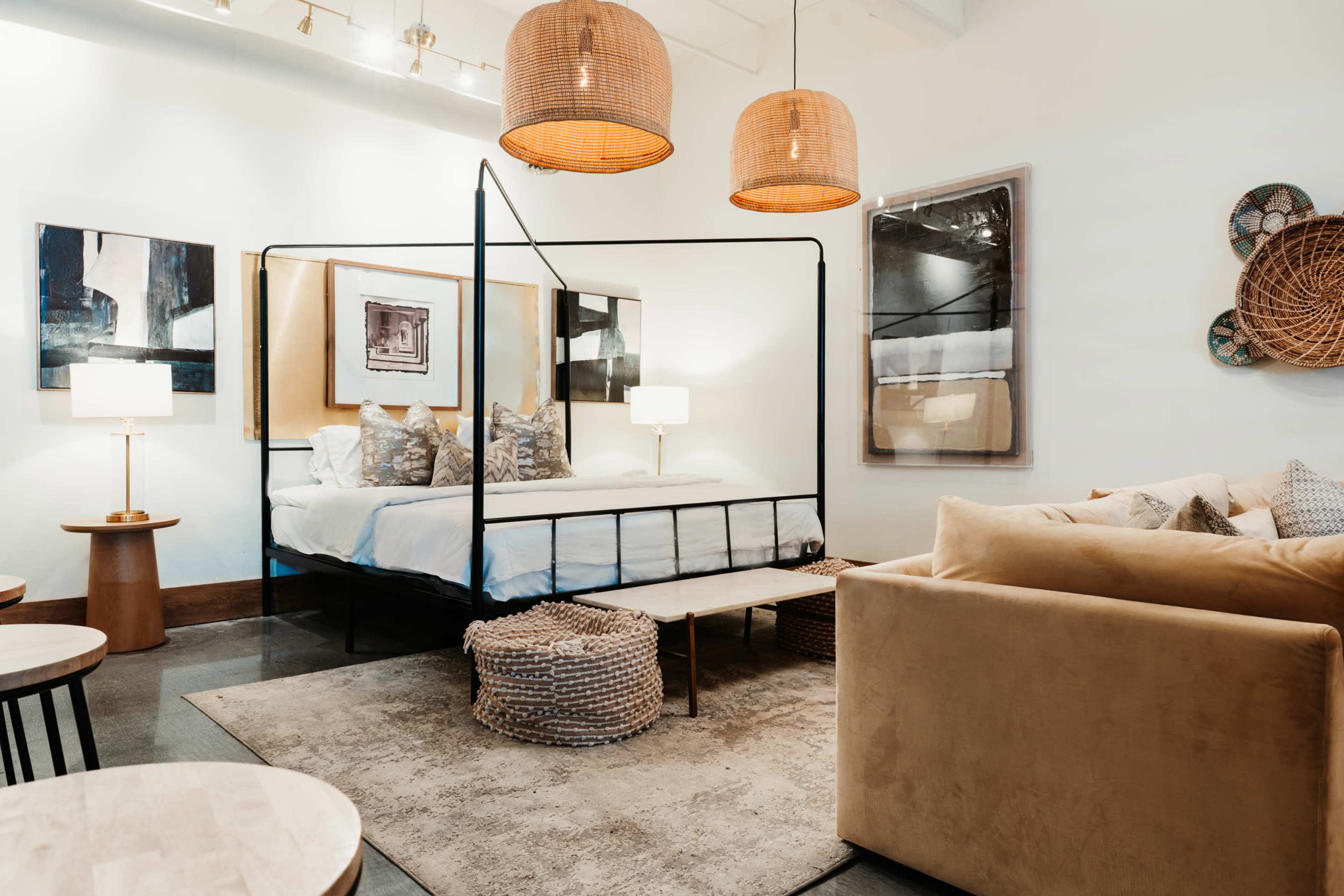 A modern bedroom setup features a black metal bed frame with a white bedding, surrounded by woven pendant lights and art on the walls.