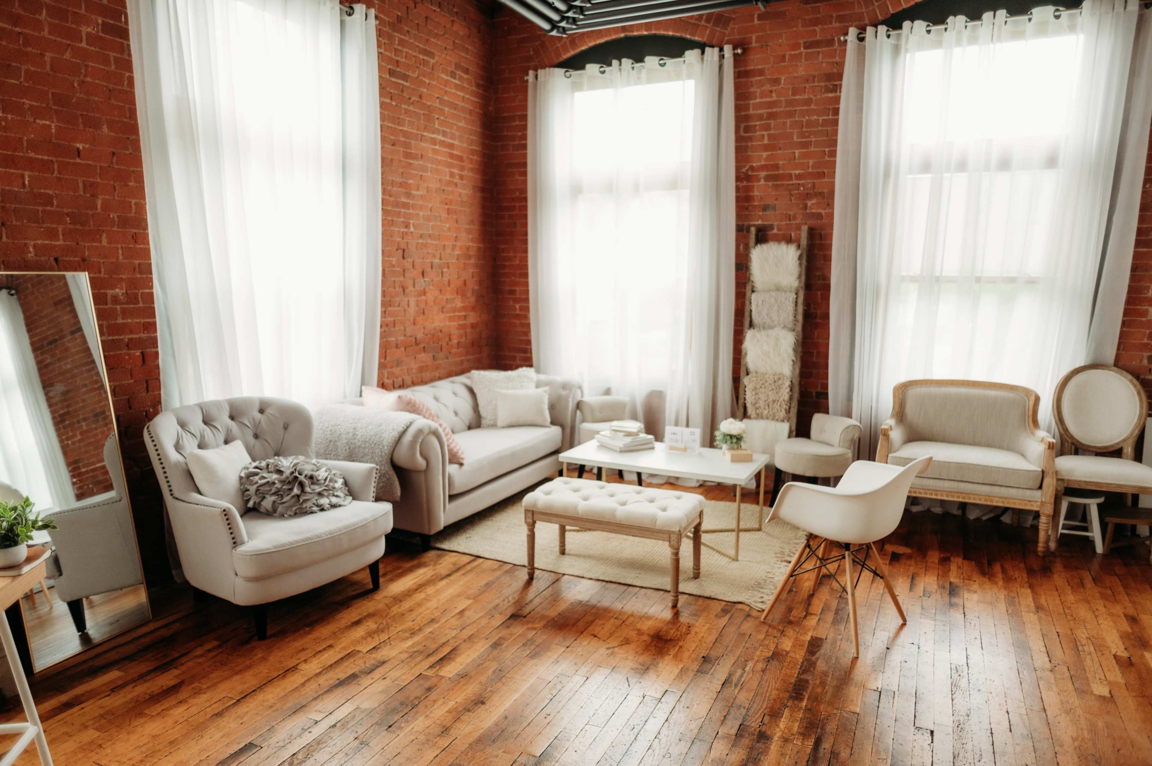 A spacious living room with exposed brick walls, large windows, and a combination of modern and vintage furniture arranged around a central coffee table.