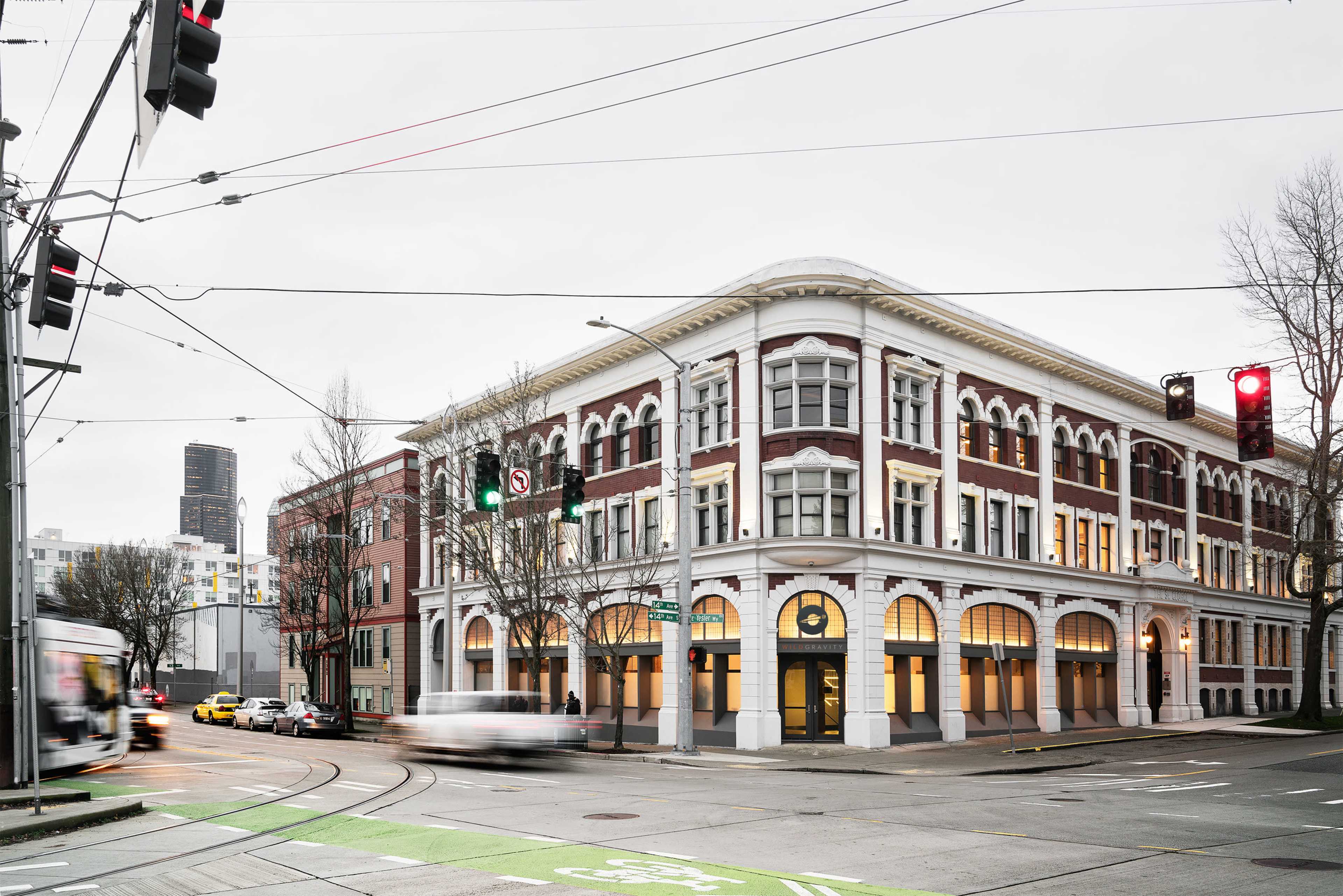 The image shows a historic red-brick building at the intersection of two streets, with traffic lights and moving vehicles in the foreground.
