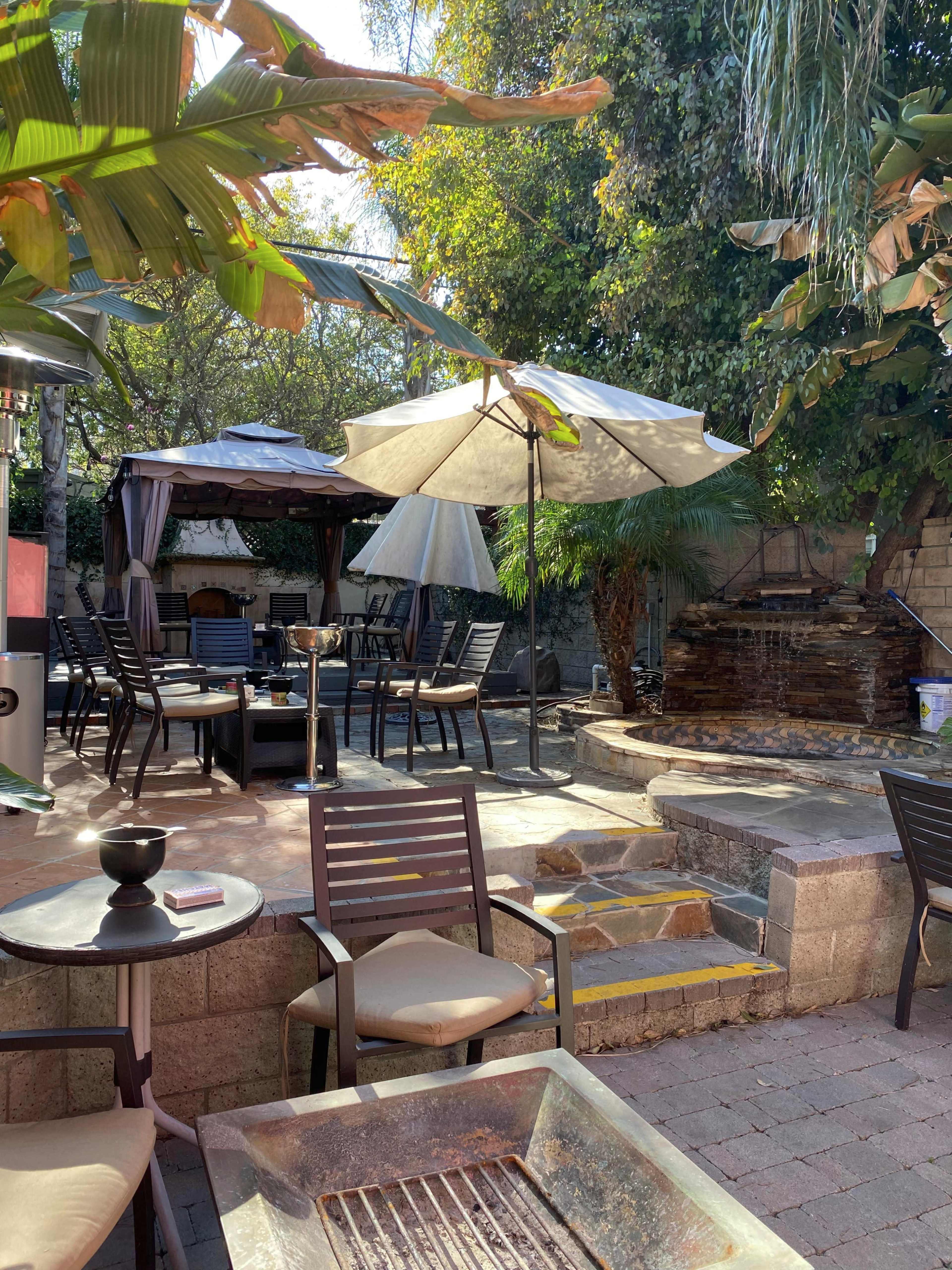 An outdoor patio area with seating, tables, a gazebo, and a water feature surrounded by greenery.