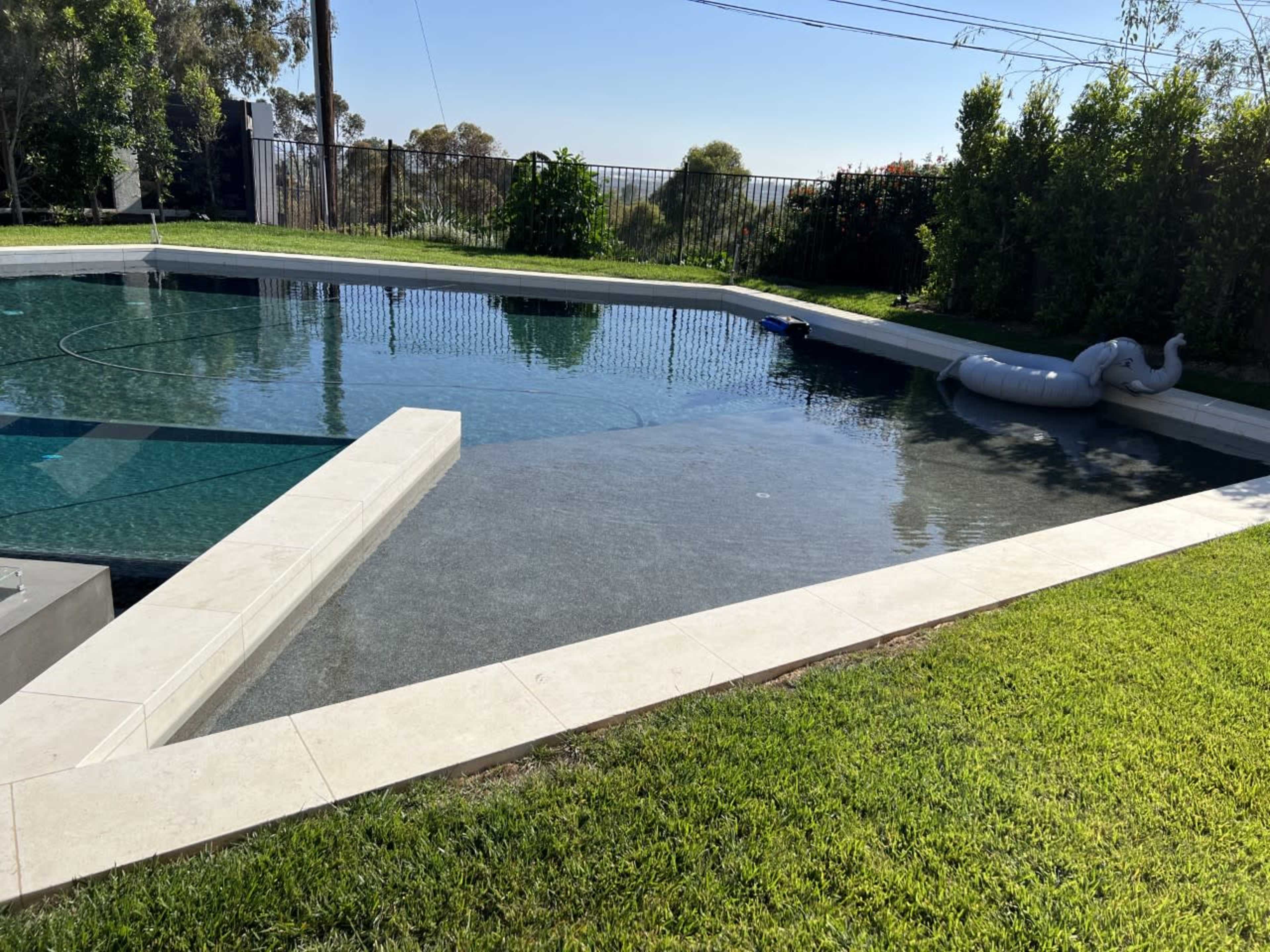 A swimming pool with clear water surrounded by a lawn and landscaping under a clear blue sky.