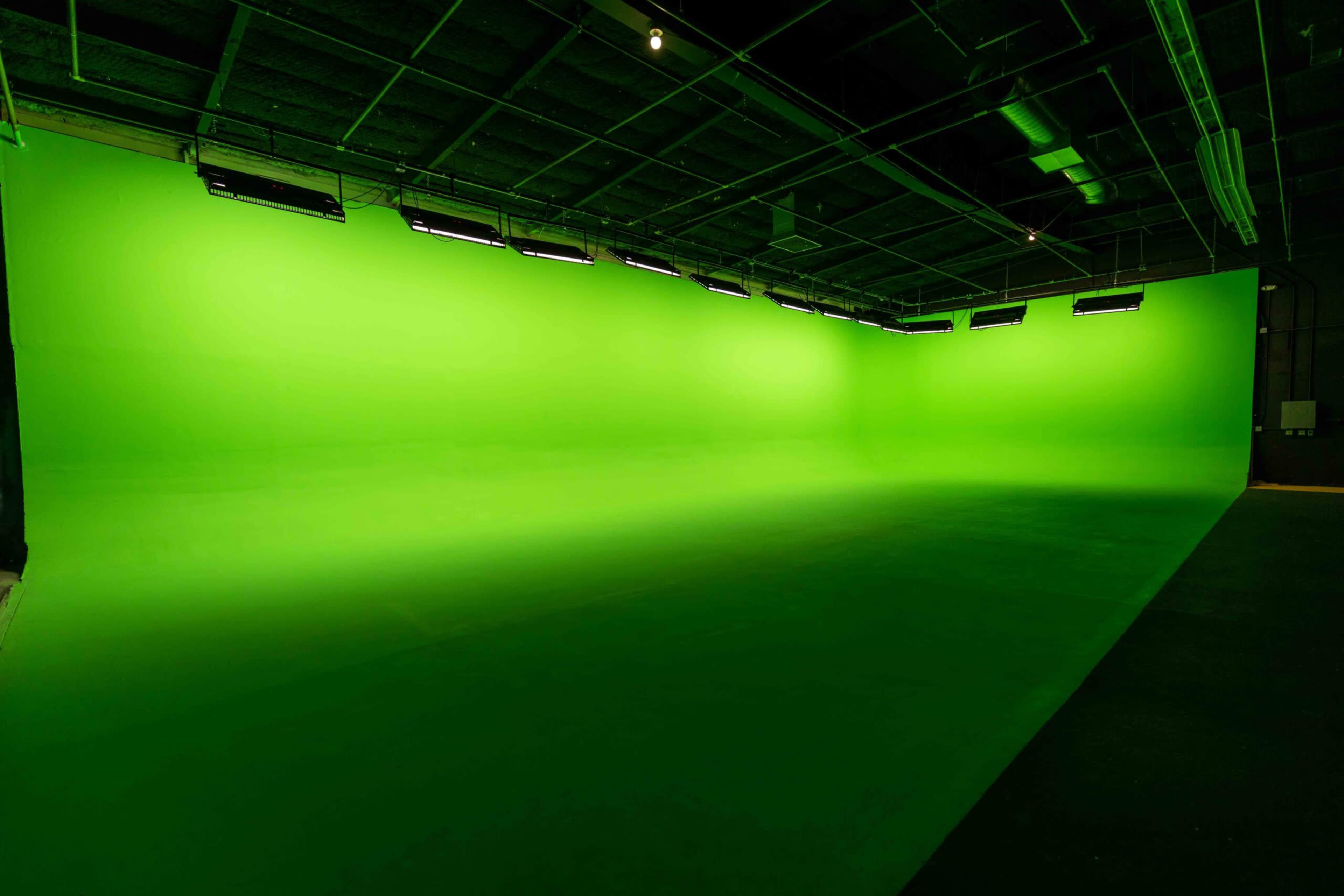 The image shows a large studio space with a bright green backdrop and overhead lighting.