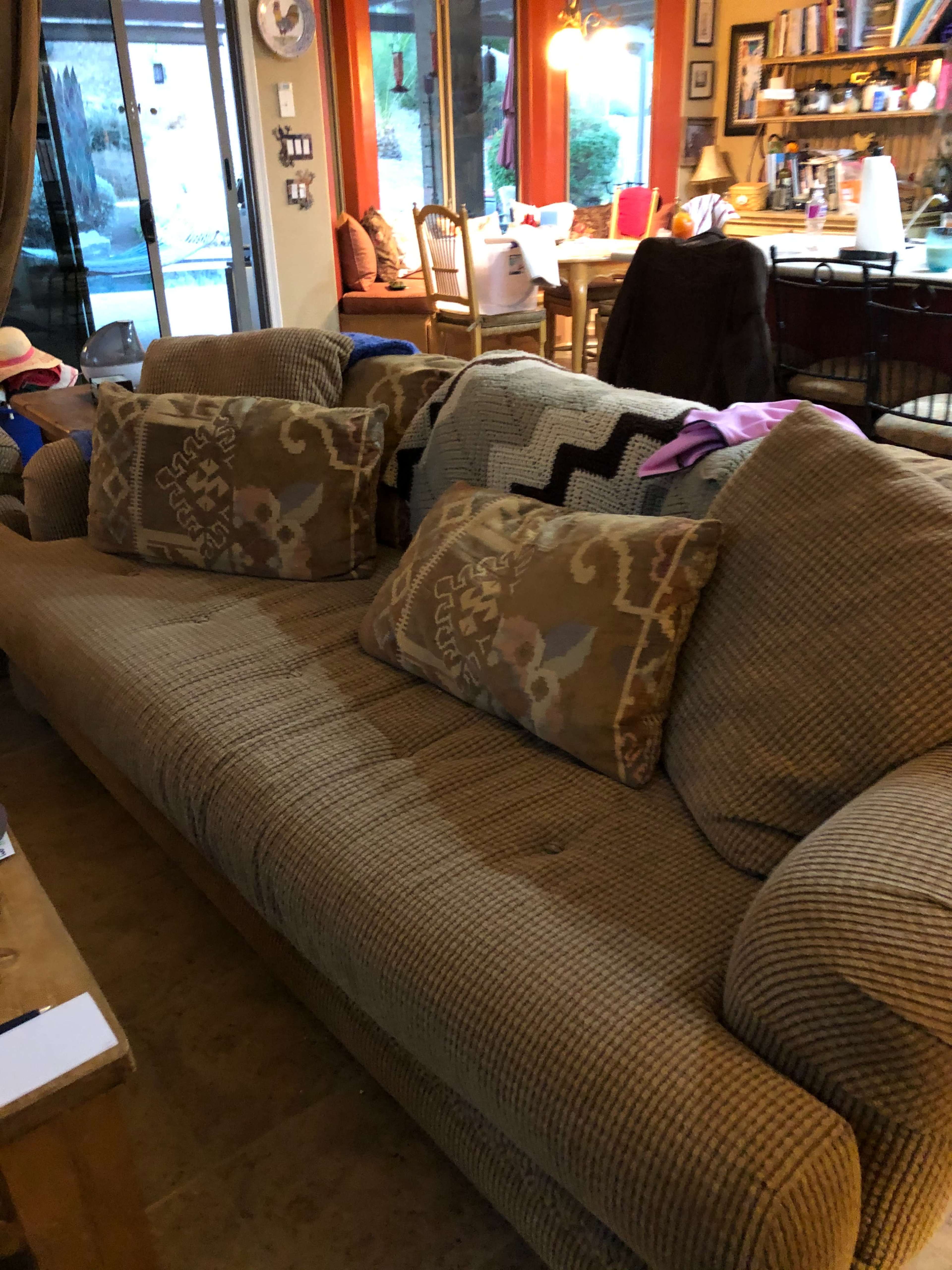 A brown couch with patterned cushions is positioned in a living room filled with various household items and furniture.