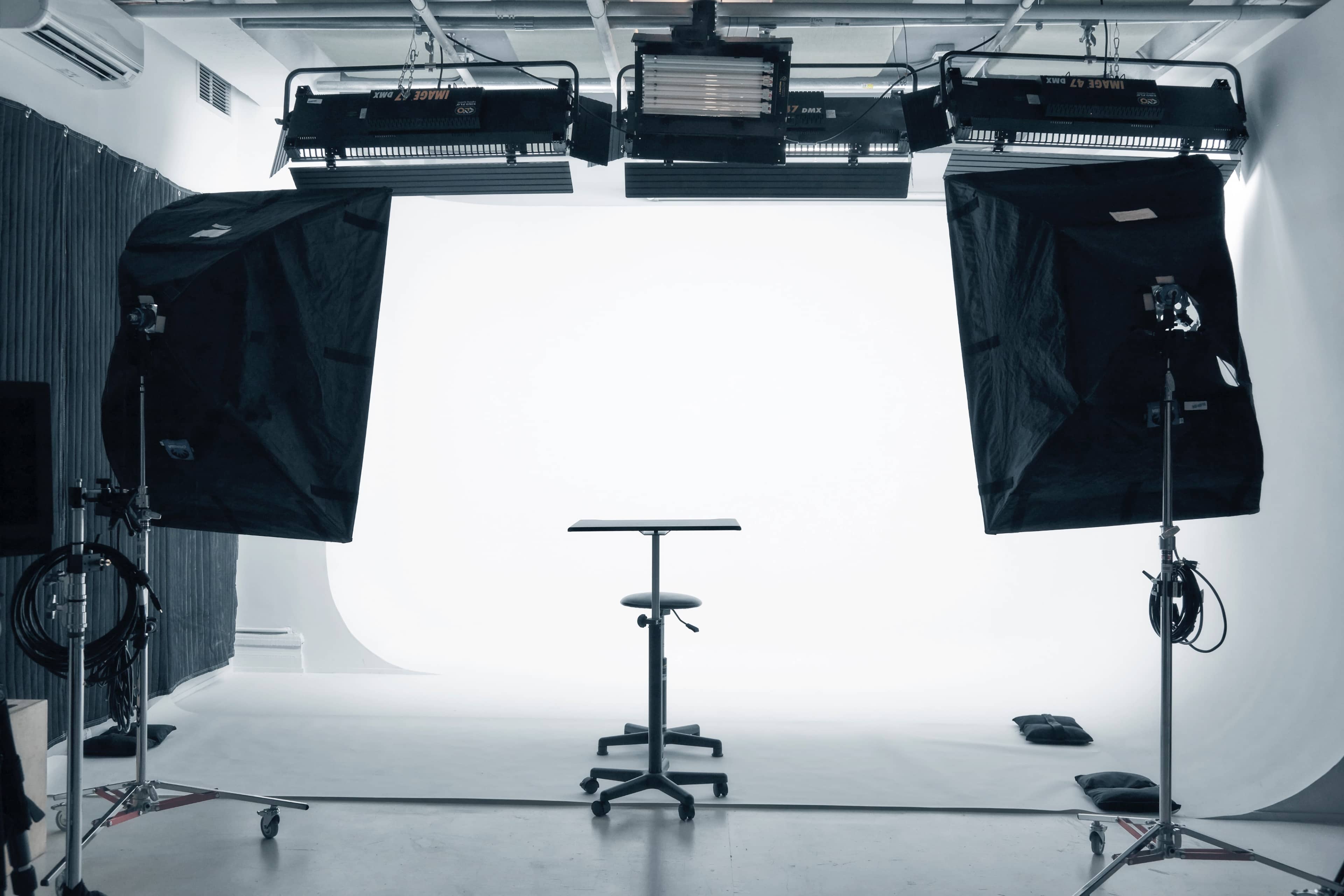 A photography studio is set up with a blank backdrop and two large lights positioned on either side of a black table and chair.