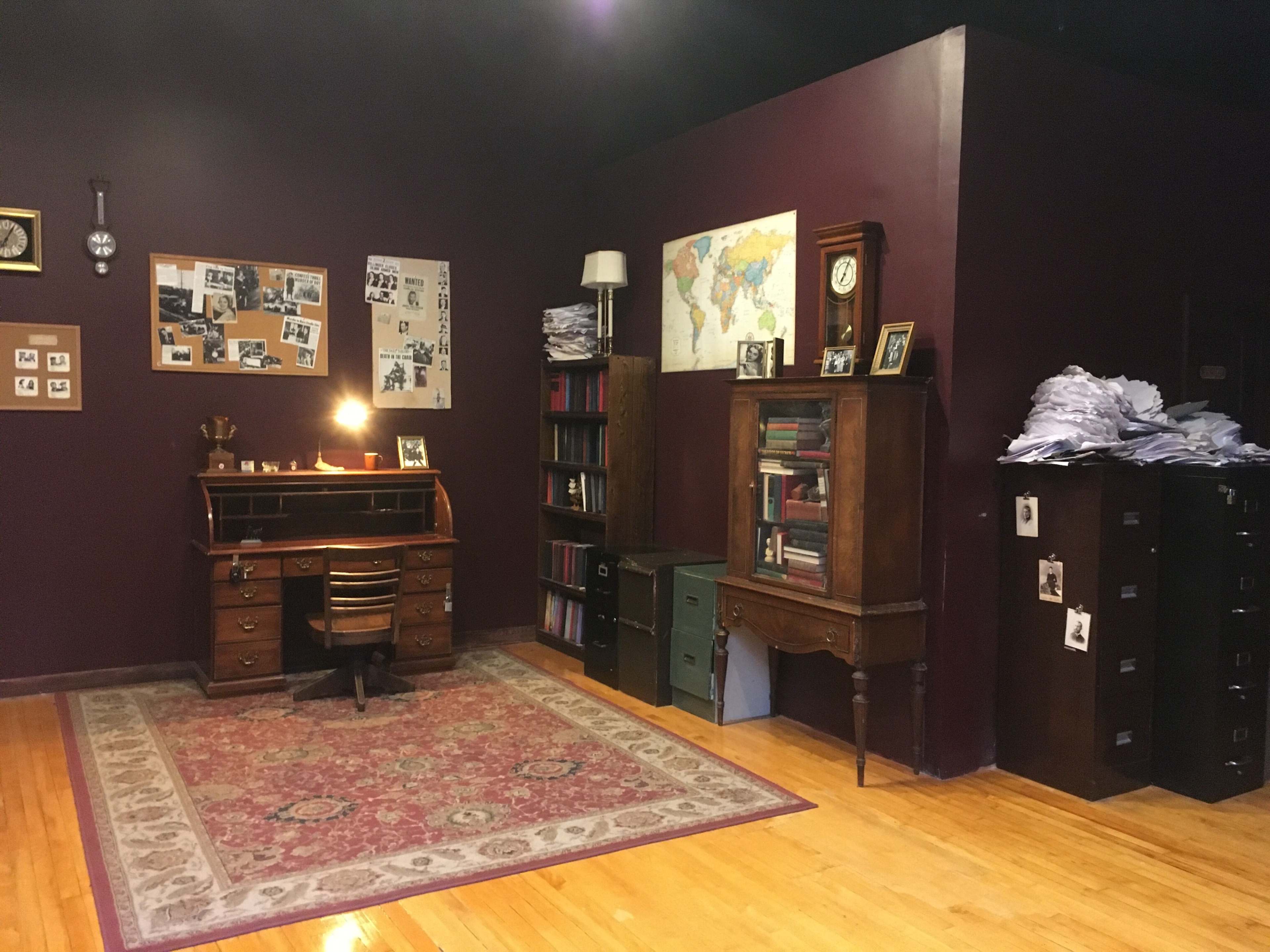 The image shows a vintage-style office with a wooden desk, a globe, bookshelves, and filing cabinets against a dark purple wall.