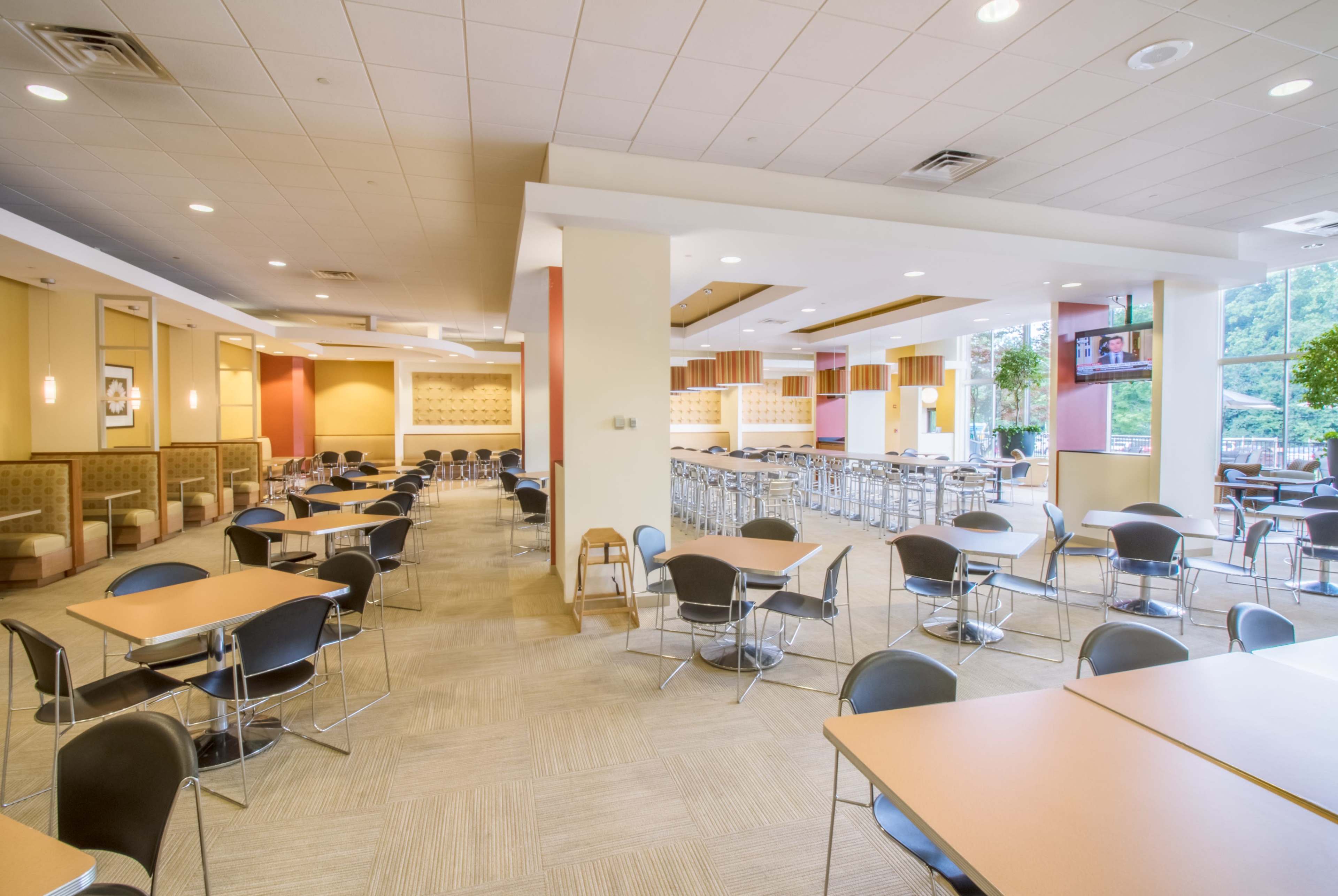 The image shows an empty dining area with tables and chairs arranged in a spacious layout, featuring both booths and standard seating.