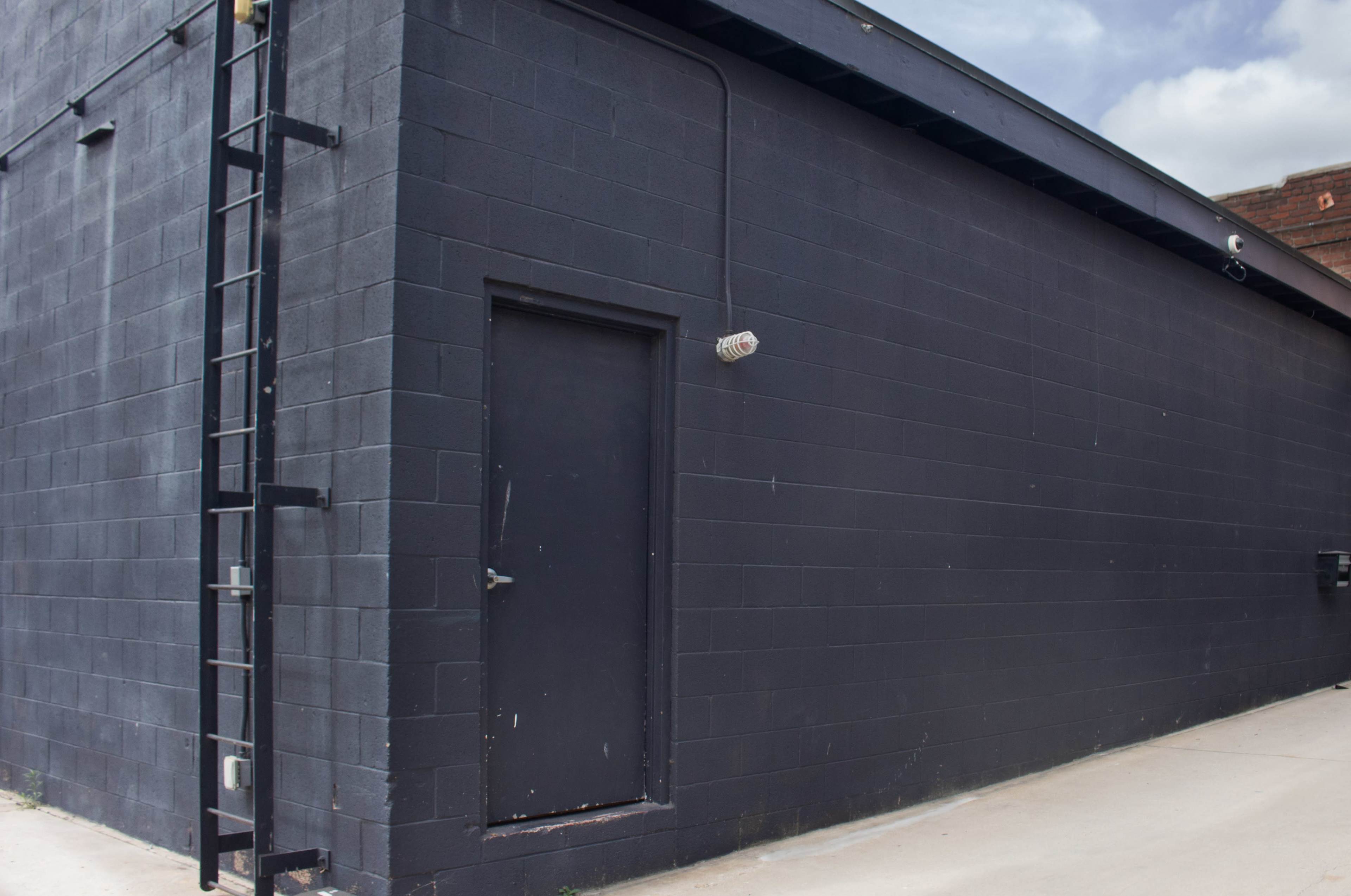 The image shows a black-painted building with a single door and a ladder on the side.