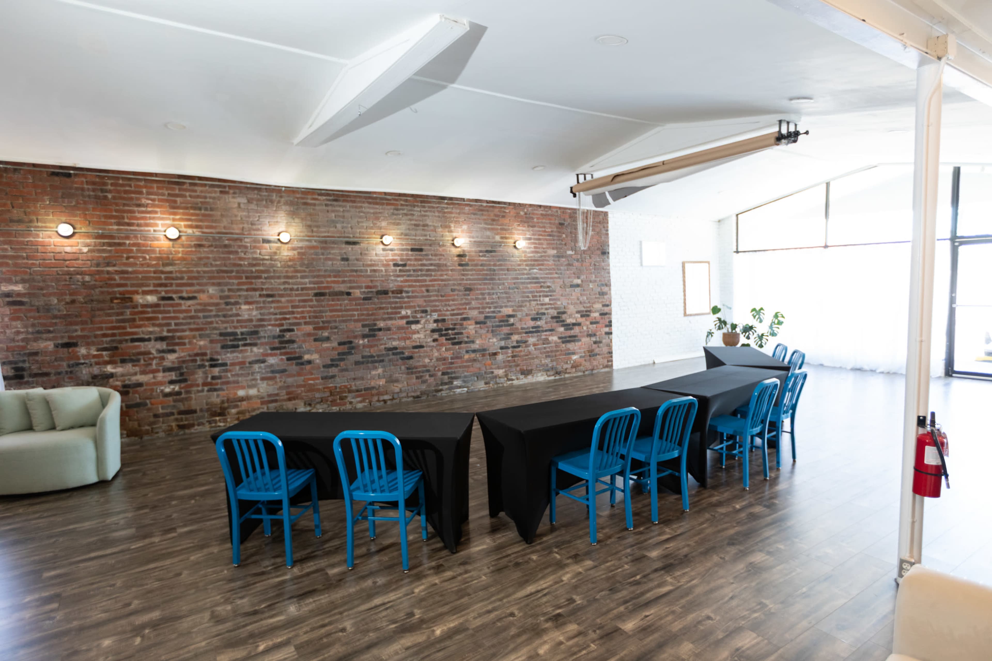 A long table with black tablecloth is set up in a spacious room with a brick wall and blue chairs around it.
