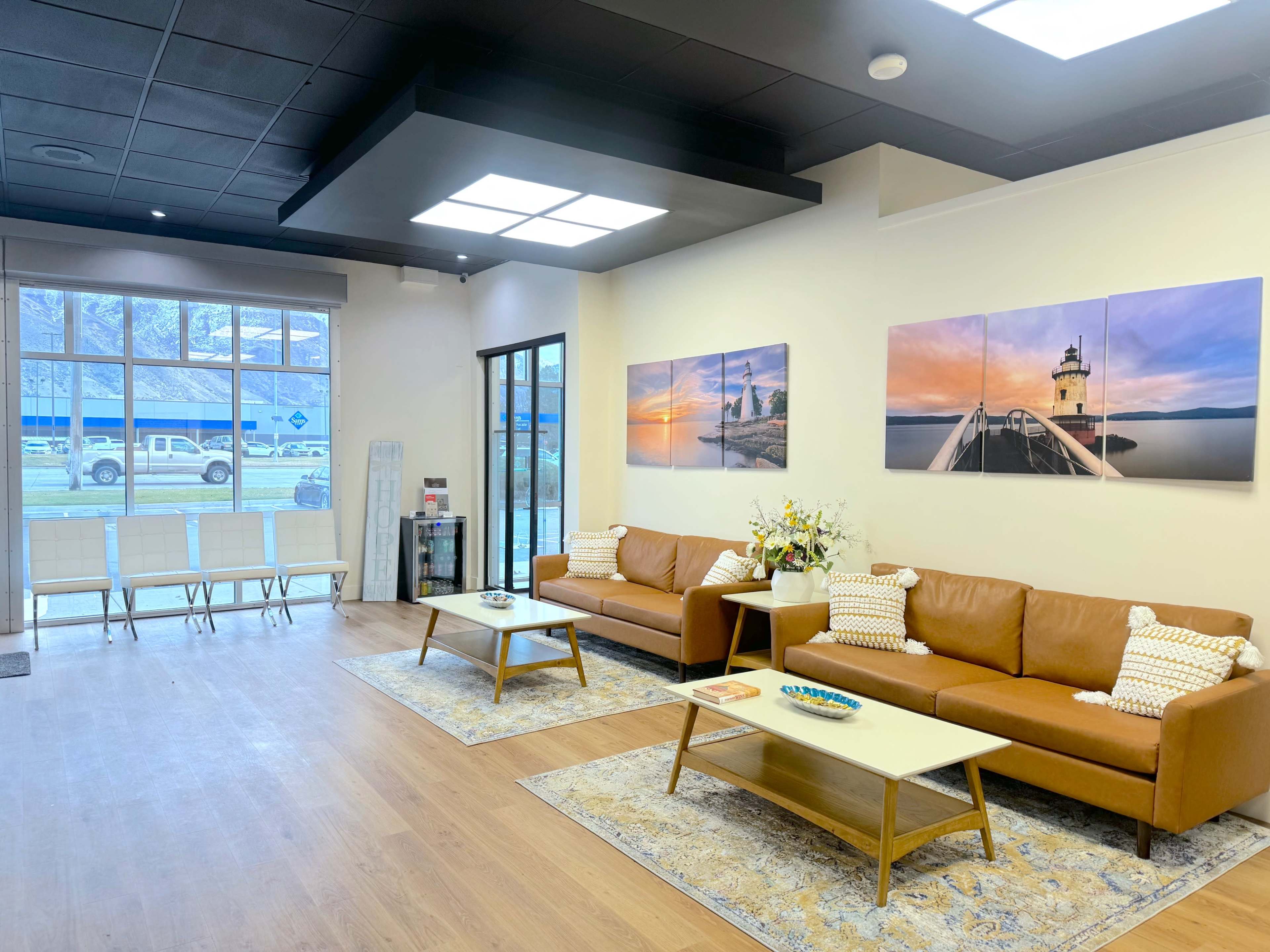 A modern waiting area with two brown leather sofas, a coffee table, and artwork depicting landscapes on the walls.