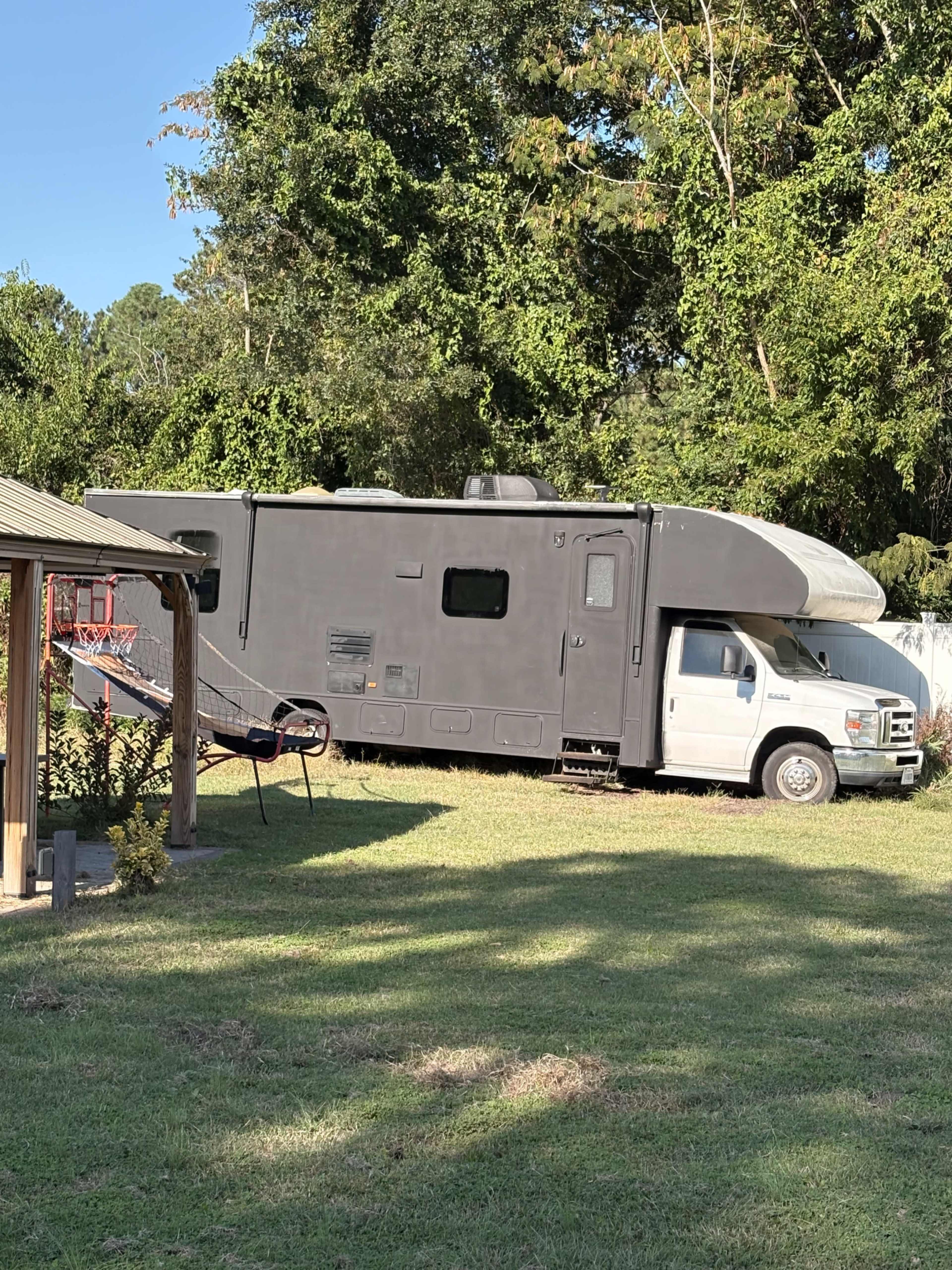 A large gray recreational vehicle is parked in a grassy area near a playground with a swing set.